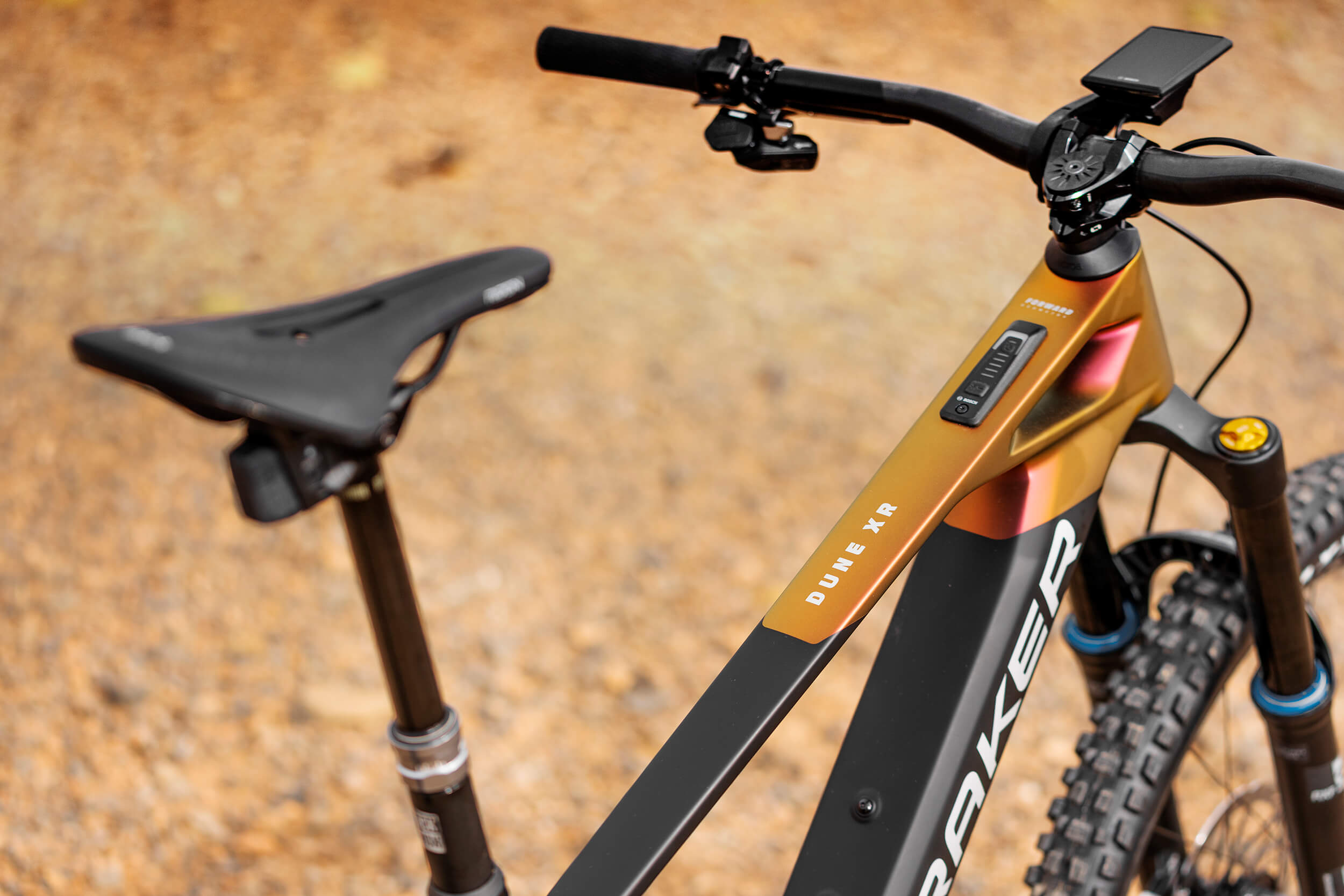 Mondraker Dune XR Mountainbike auf Schotterweg, Fokus auf Sattel, Lenker und Rahmen in Schwarz und Bronze.