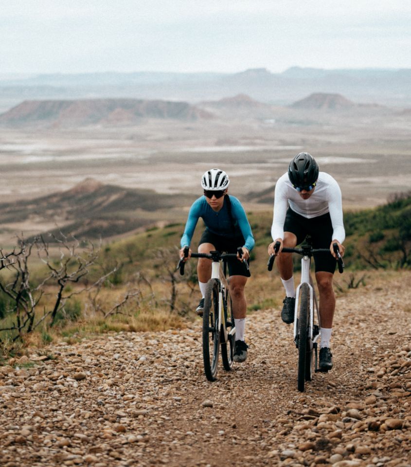 Zwei Radfahrer auf Schotterweg mit Orbea Terra Fahrrädern, tragen Helme und Sportkleidung, in bergiger Landschaft.