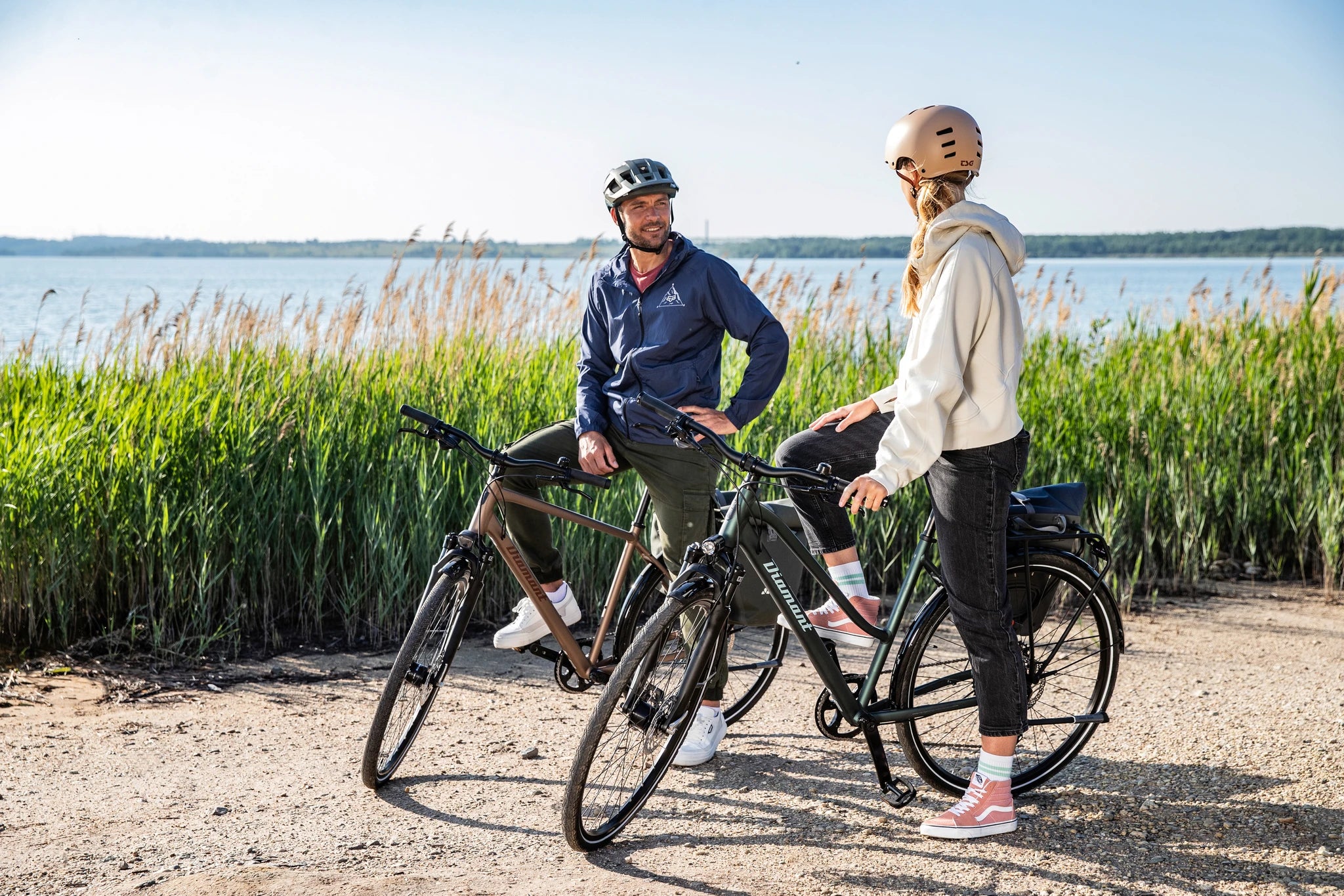 Zwei Personen mit Helmen auf Diamant-Fahrrädern in der Natur, im Hintergrund Schilf und ein See.