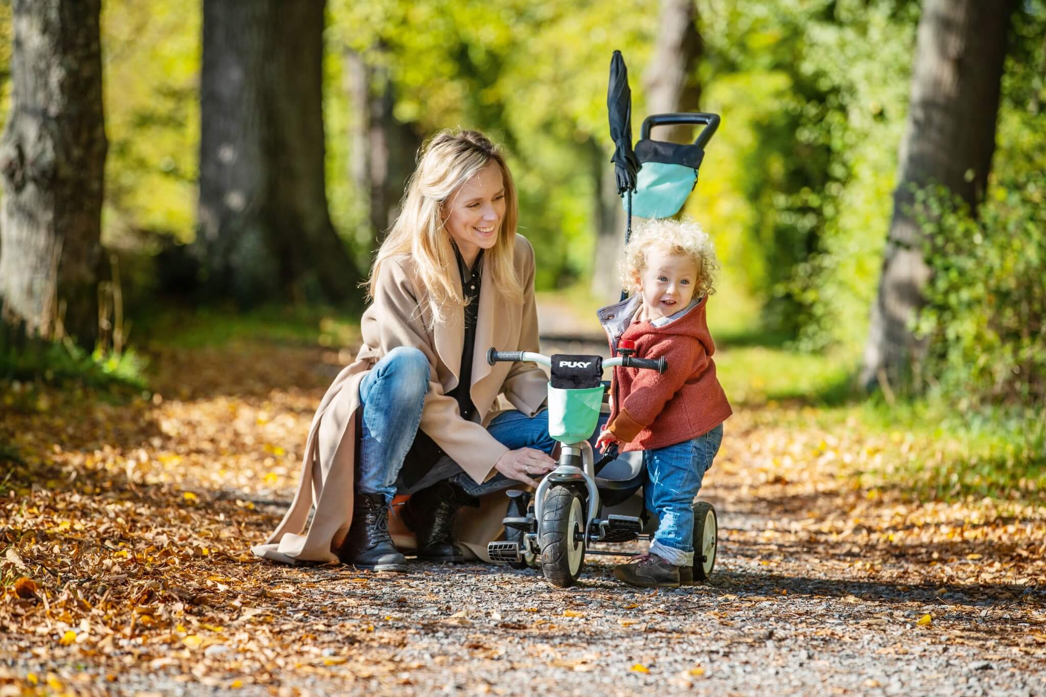 Mutter und Kind mit Puky Dreirad im Park auf Herbstweg, ideal für Kleinkinder.