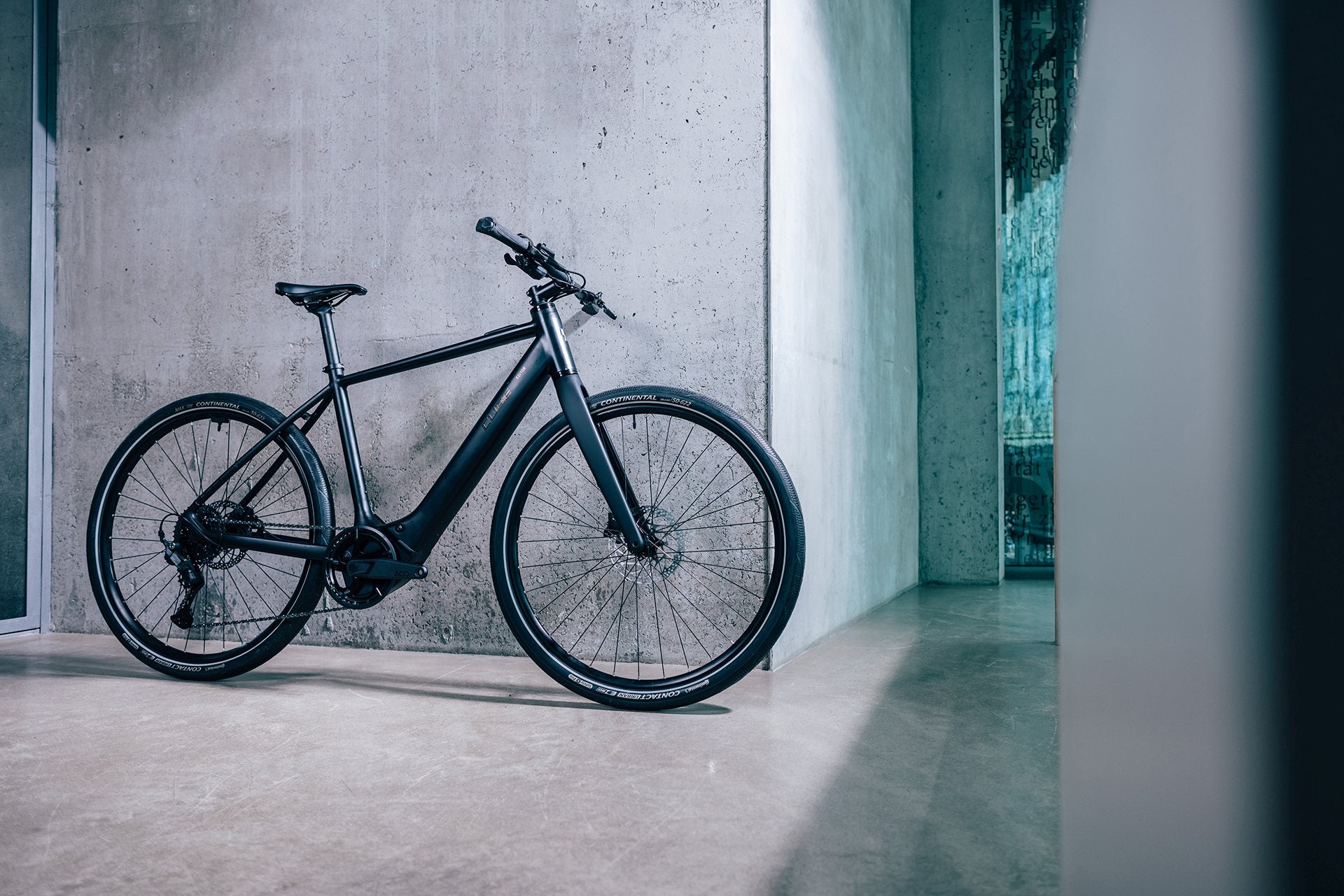 Schwarzes E-Bike Cube Editor Hybrid lehnt an Betonwand, schlankes Design, geeignet für urbane Pendler.