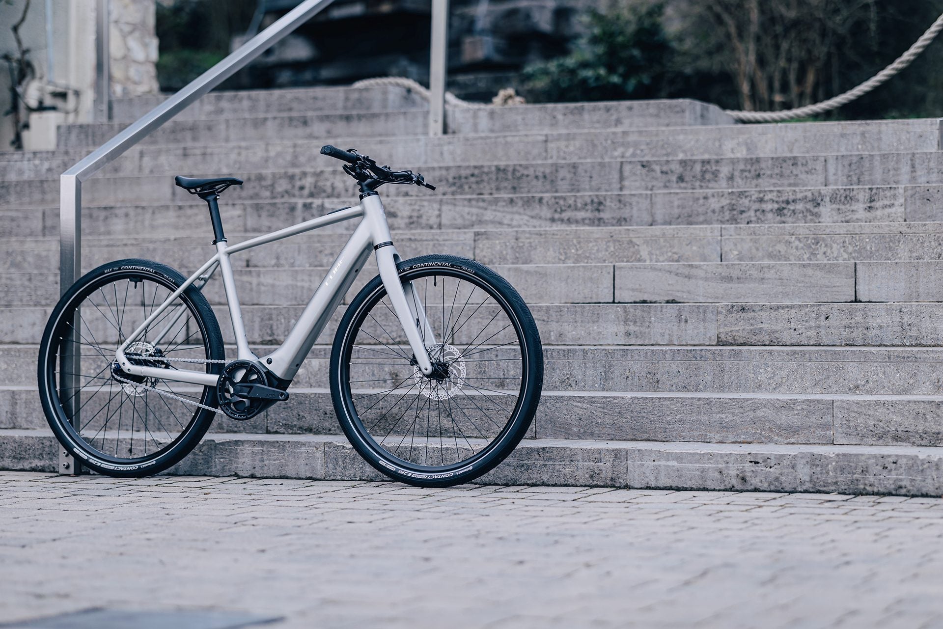 Graues Cube Hybrid-Fahrrad lehnt an einer Treppe, geeignet für urbane Fahrer, mit schwarzen Reifen und schlankem Design.
