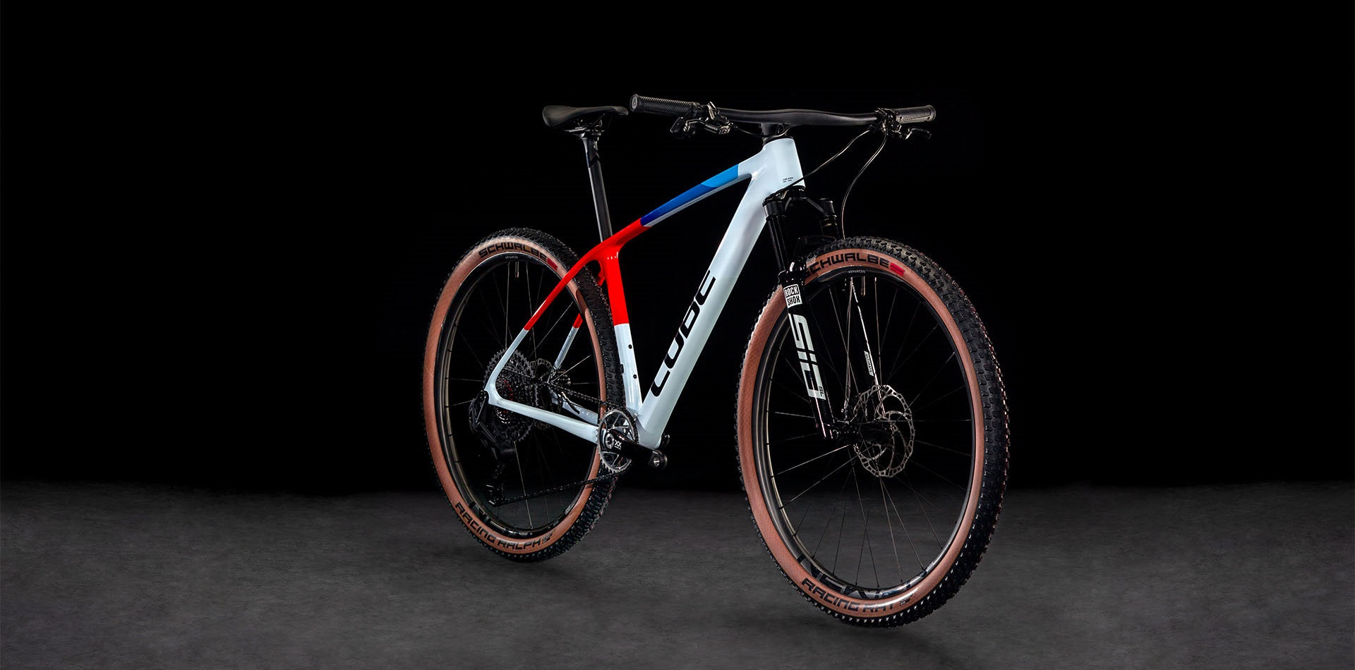 Modernes Cube-Mountainbike in Weiß, Rot und Blau, geeignet für Offroad-Abenteuer; RockShox-Gabel, Schwalbe-Reifen.