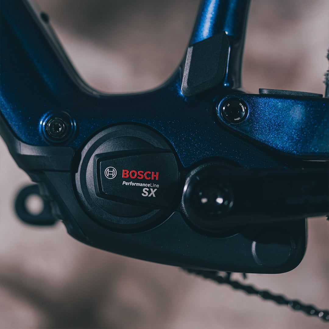 Nahaufnahme eines Bosch Performance Line SX E-Bike-Motors, montiert an einem blauen Fahrradrahmen.