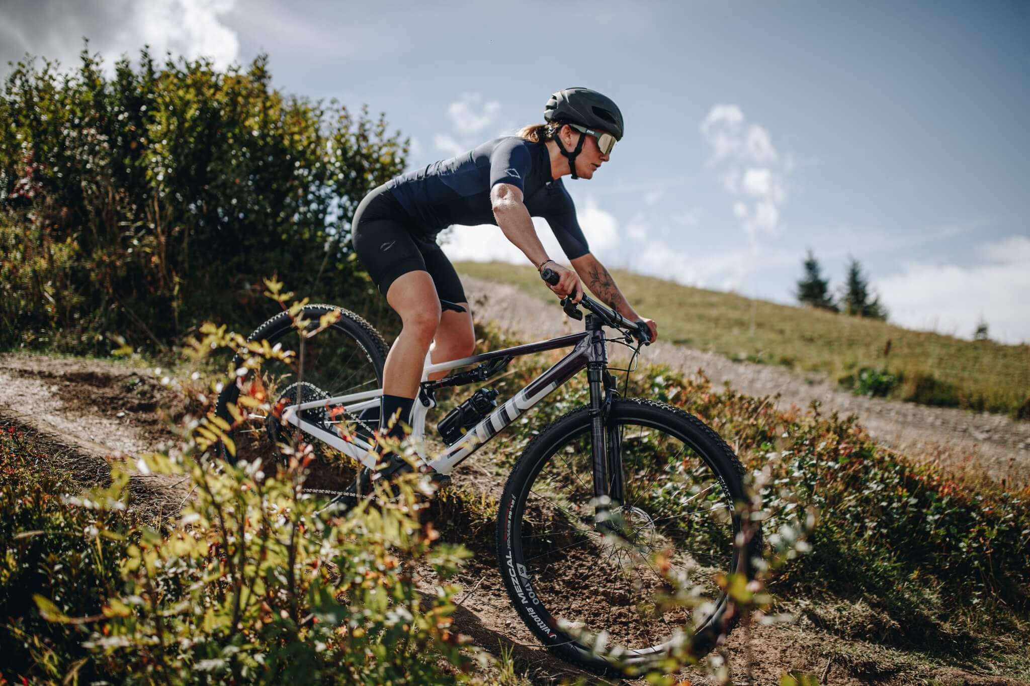Person fährt ein BMC Mountainbike auf einem Waldpfad bergab, trägt Helm und Sportbekleidung.