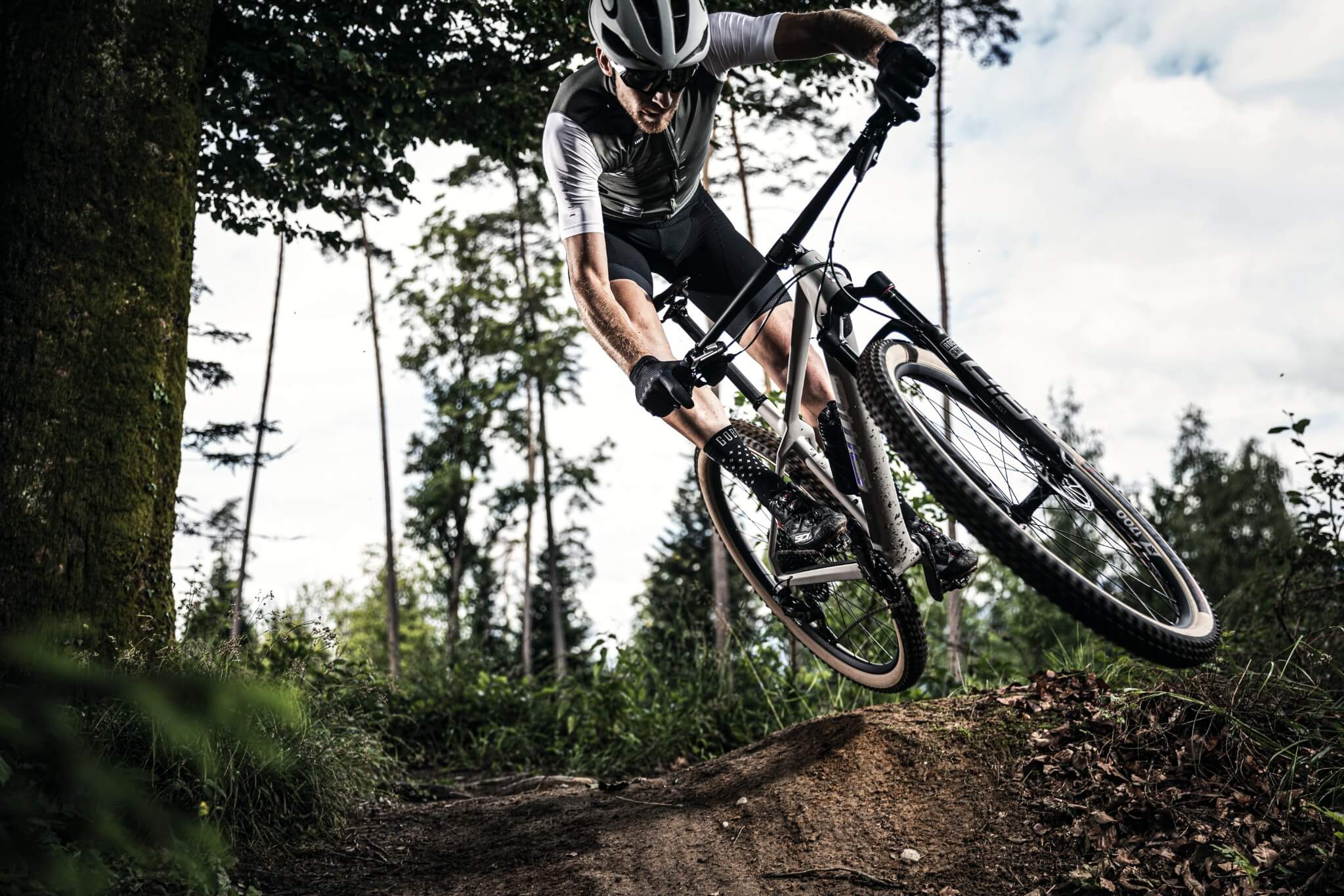 Mountainbiker mit Helm auf einem BMC TwoStroke Fahrrad springt über eine Erdhügel im Wald.