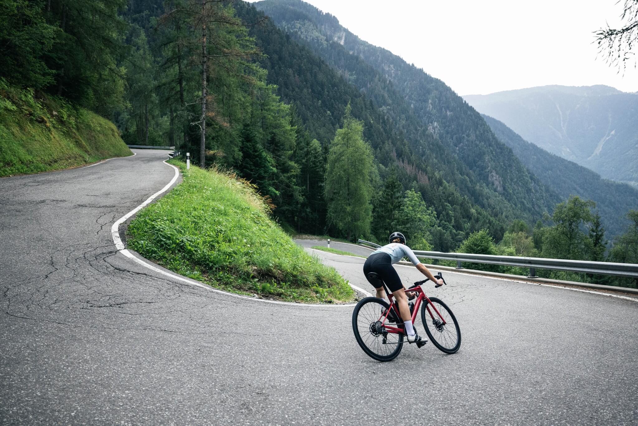 Radfahrer mit BMC-Rennrad fährt auf kurviger Bergstraße durch bewaldete Landschaft.