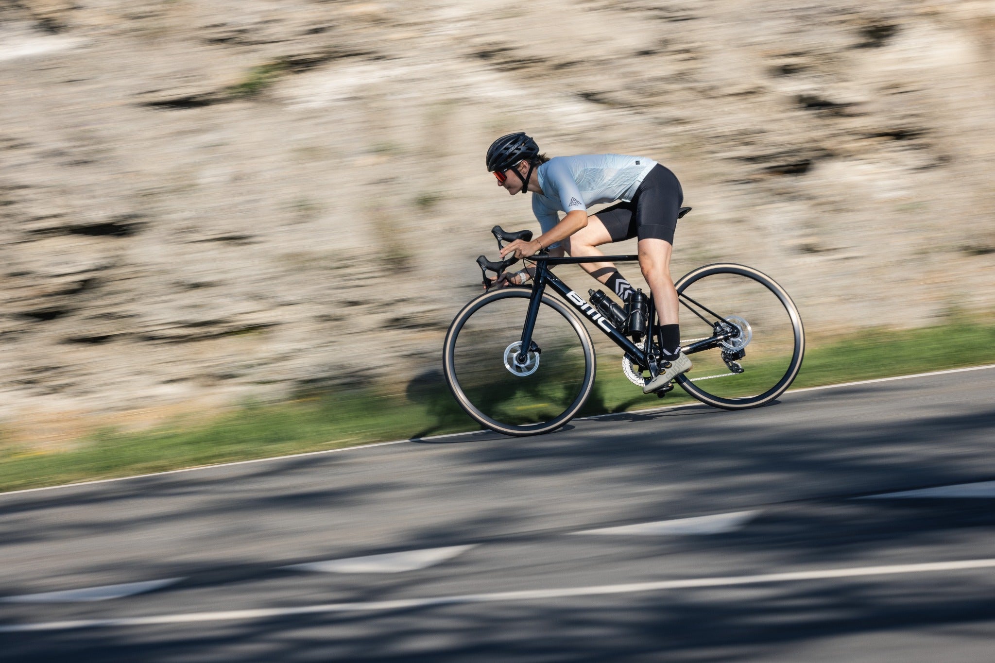 Person auf BMC-Rennrad fährt schnell auf einer kurvigen Straße, trägt Helm und sportliche Kleidung.