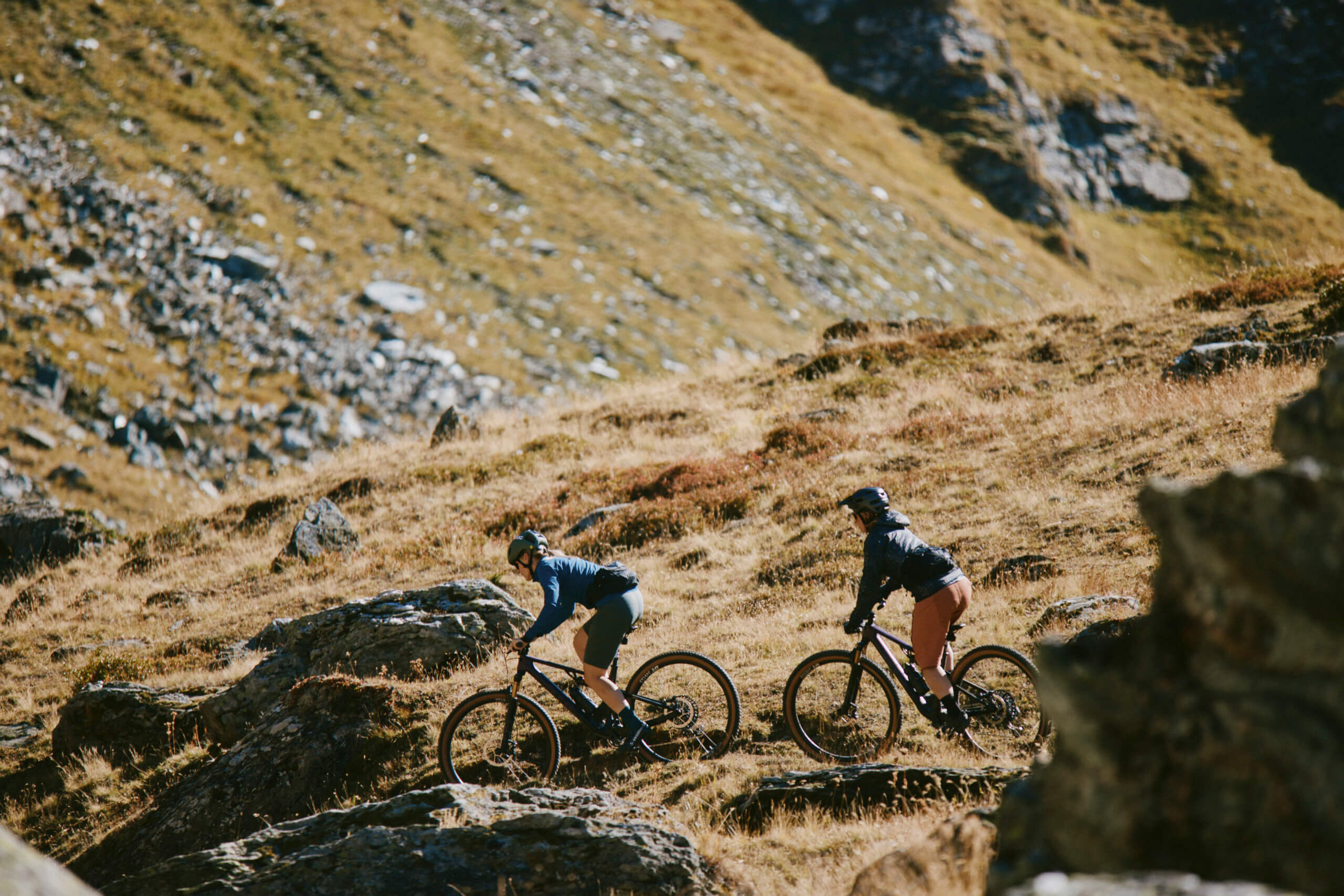 Zwei Personen fahren auf BMC Fourstroke Mountainbikes über einen felsigen Hügelpfad in einer natürlichen Landschaft.