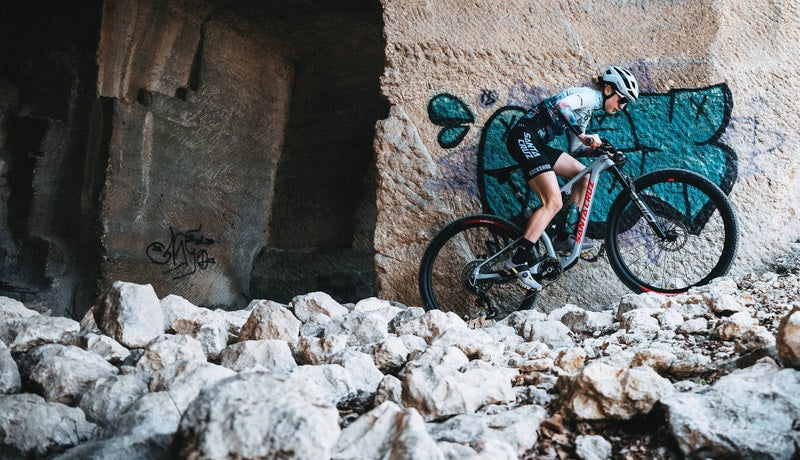 Sportler auf Santa Cruz Mountainbike fährt steiniges Gelände mit Helm und Trikot. Graffiti im Hintergrund.