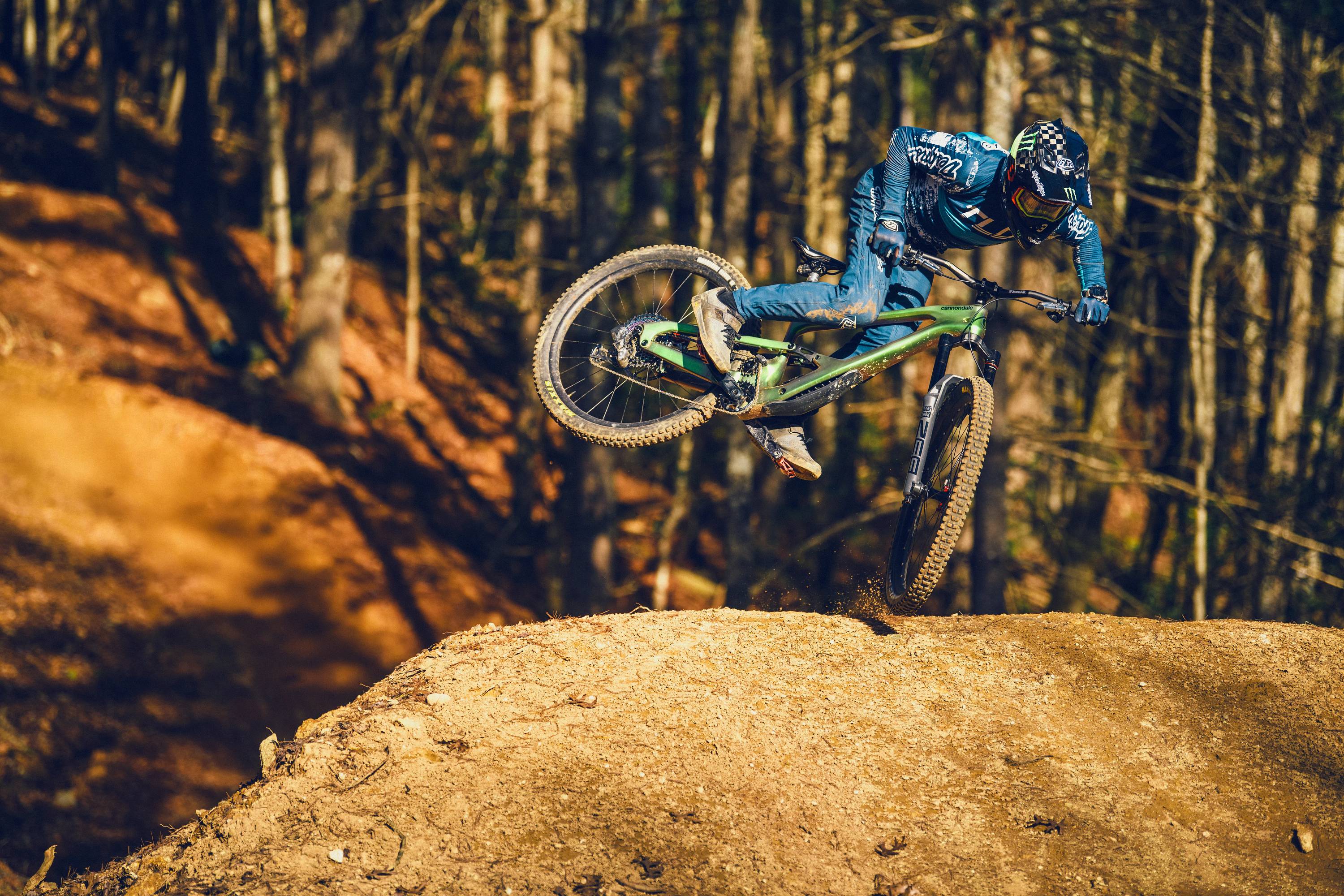 Mountainbiker springt im Wald mit grünem Cannondale-Bike über einen Hügel.