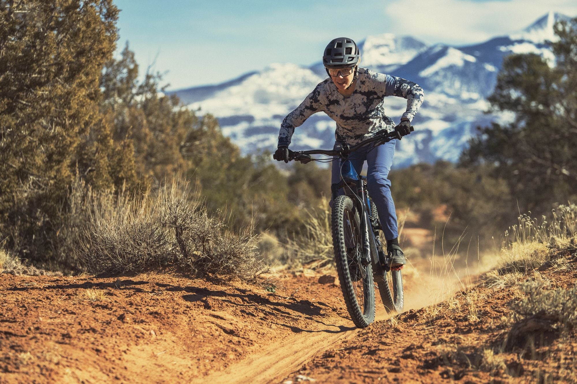 Person fährt Cannondale Hardtail-Mountainbike auf einem Waldweg, im Hintergrund Berge.