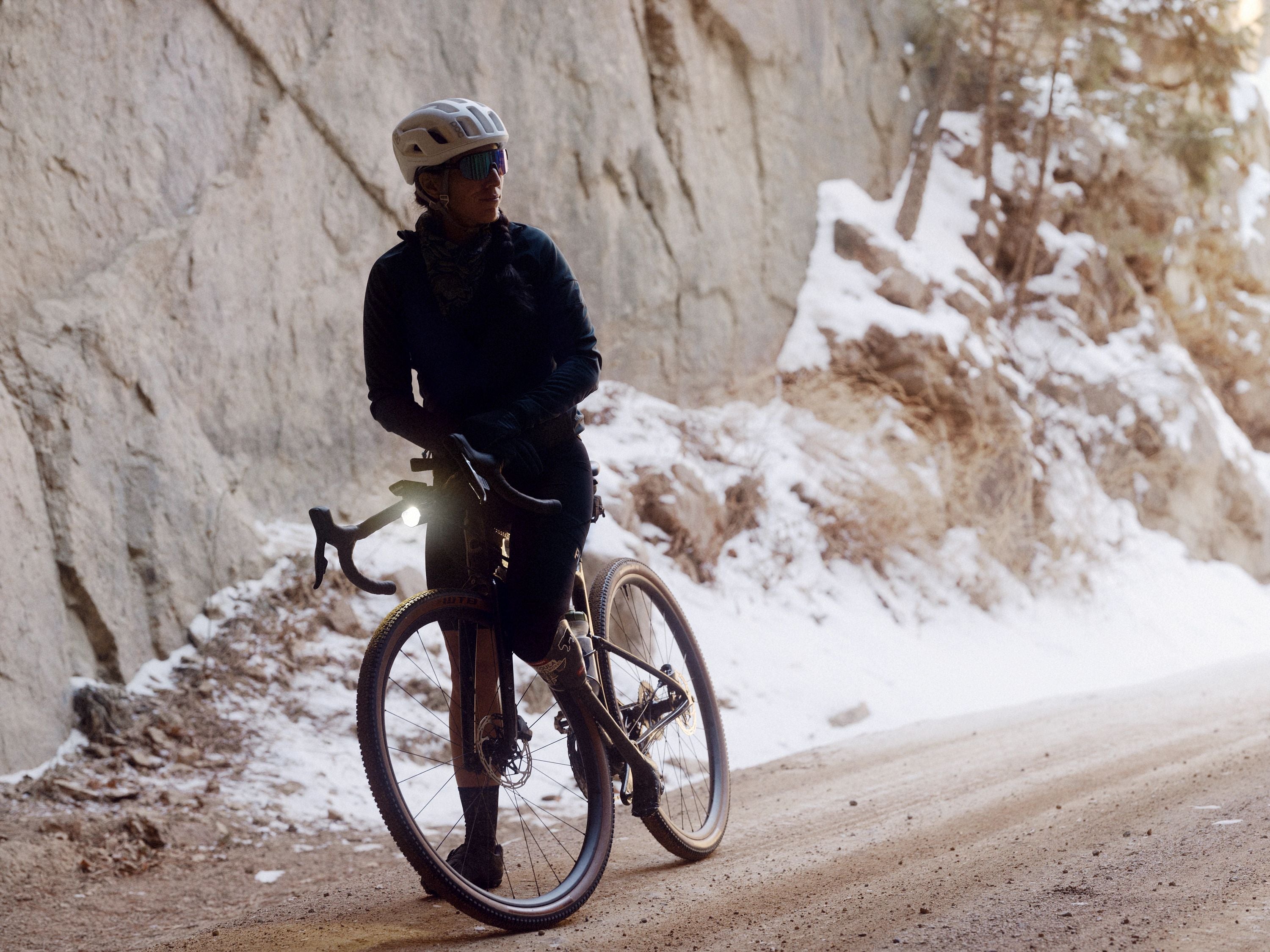 Person mit Helm auf einem Cannondale Topstone Fahrrad bei winterlicher Straße in bergiger Landschaft.