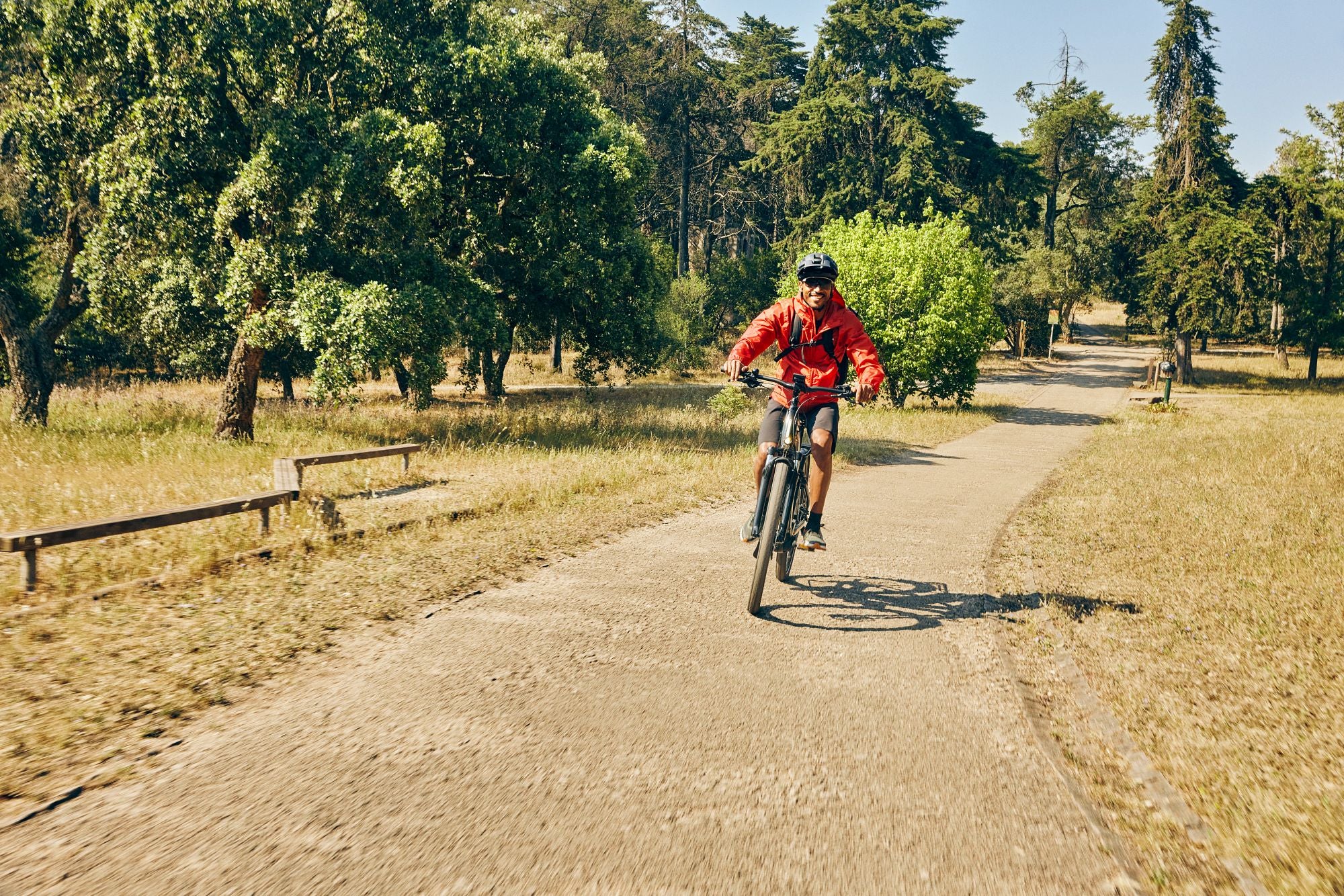 Person auf einem Cannondale E-Bike fährt auf einem Weg durch einen sonnigen Park, umgeben von Bäumen und Wiese.
