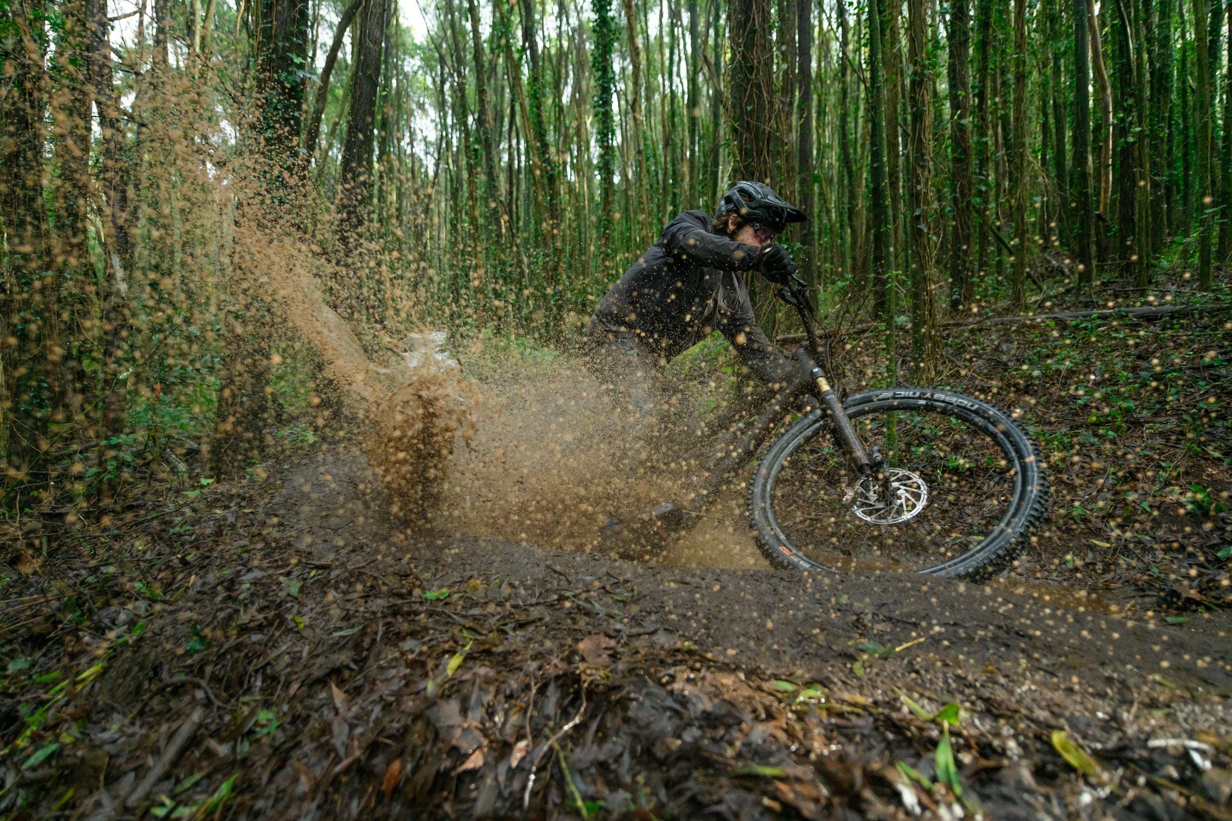 Fahrradfahrer in voller Fahrt durch matschigen Wald, mit Schutzhelm und Mountainbike.