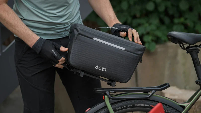 Fahrradtasche von ACID wird an einem Gepäckträger montiert; ideal für Radfahrer zur sicheren Aufbewahrung von Gegenständen.