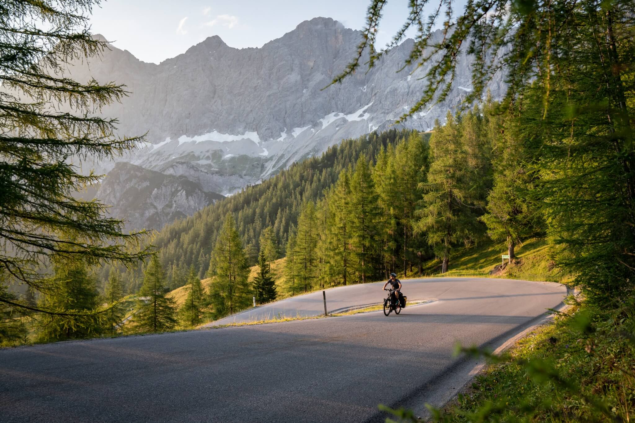Person auf Haibike e-Trekkingrad in malerischer Berglandschaft aus Straße, Wald und Bergen.