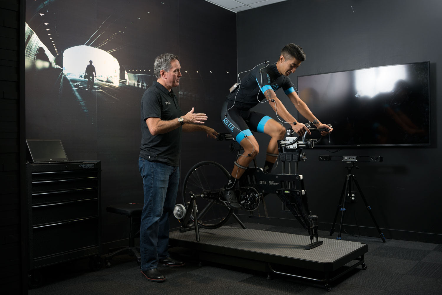 Radfahrer auf RETÜL Bikefitting-Rig, betreut von Experten in modernem Studio, für optimale Fahrradeinstellung.