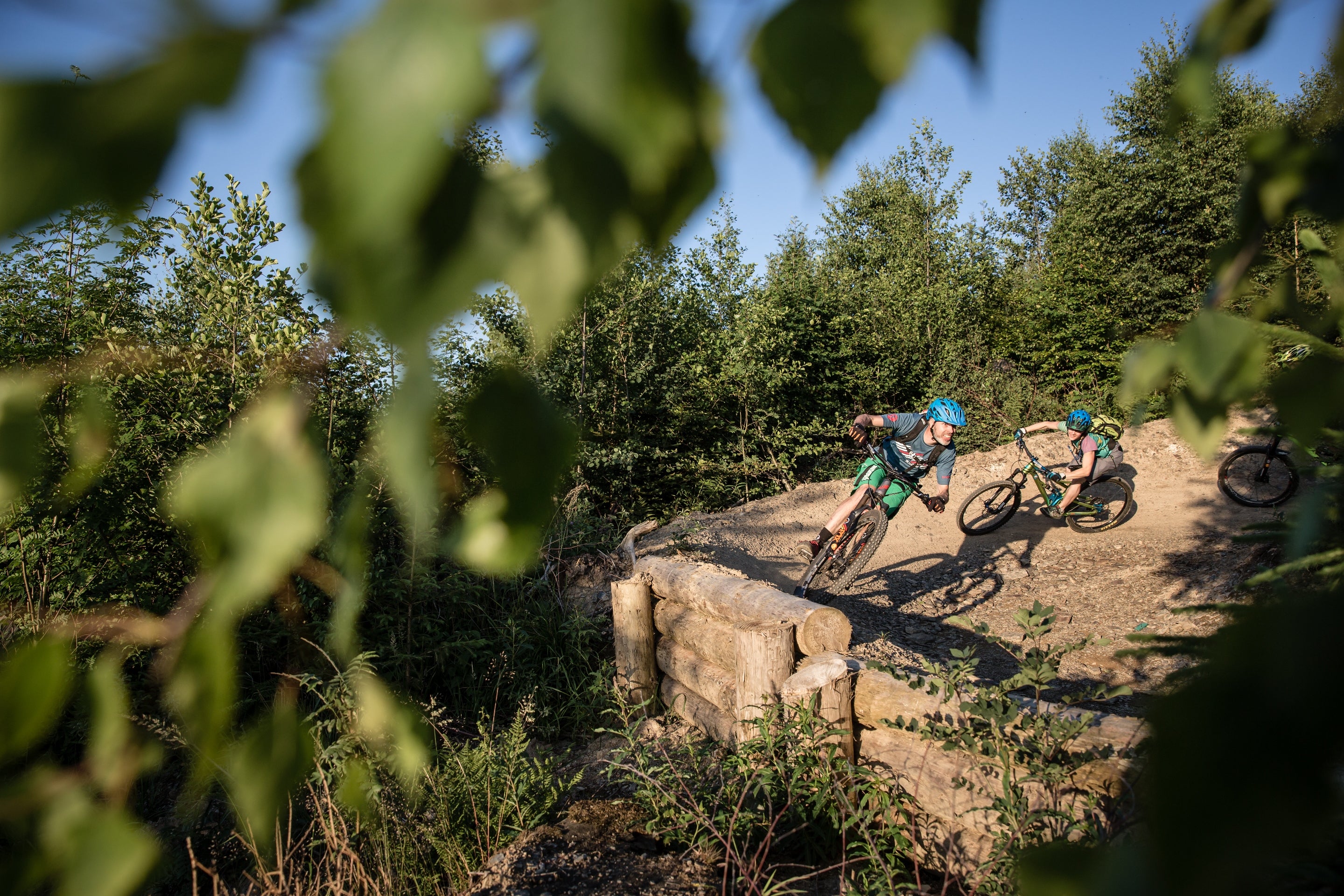 Mountainbiker fahren kurvigen Waldpfad entlang, umgeben von grünen Bäumen, bei sonnigem Wetter.