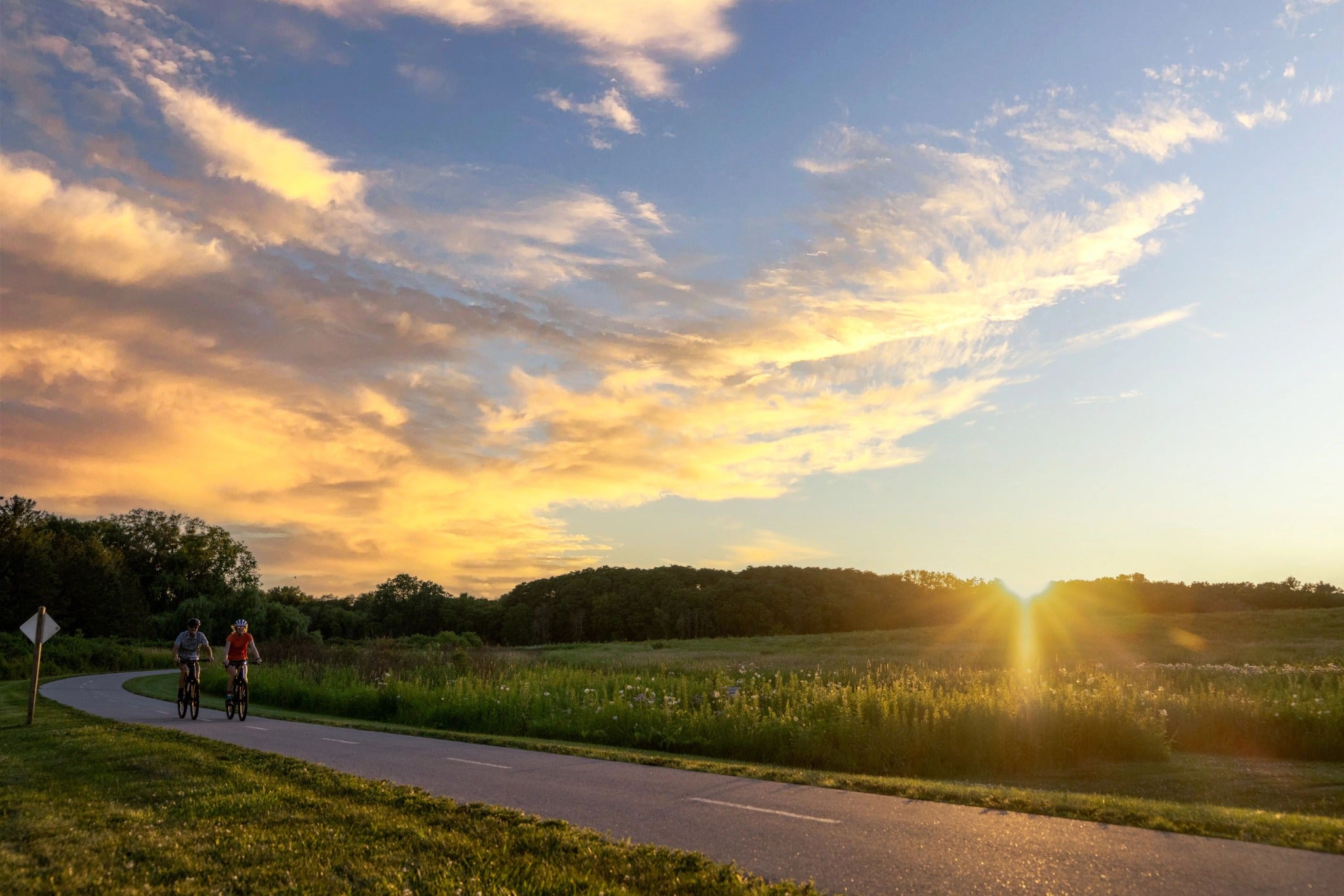 Zwei Radfahrer auf einem Weg bei Sonnenuntergang in einer ländlichen Landschaft.
