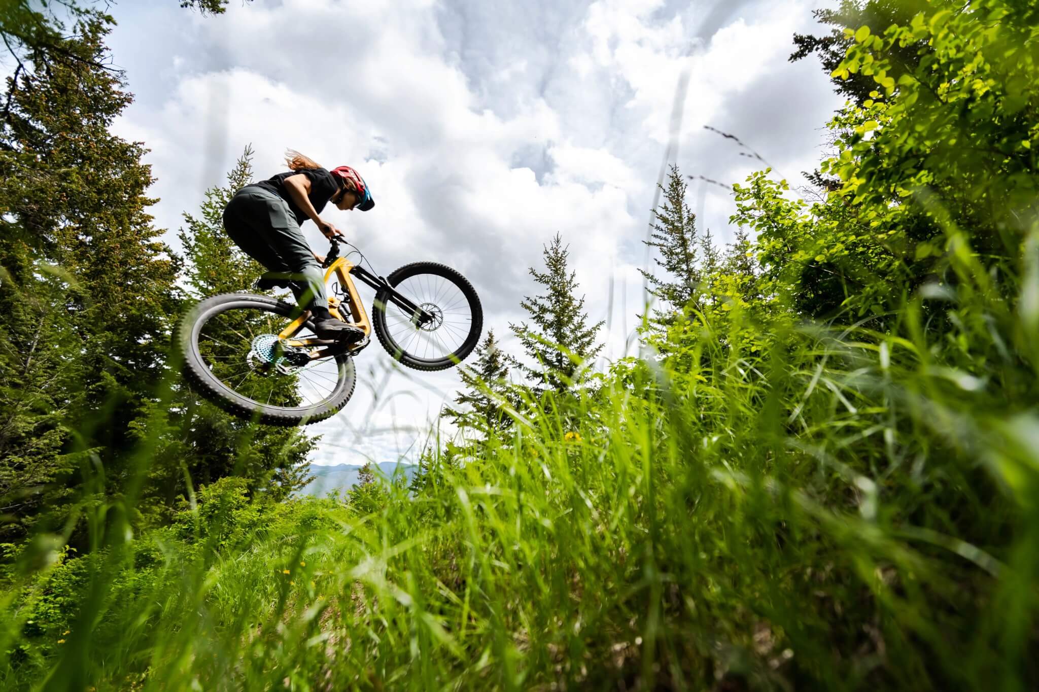 Fahrradfahrer auf gelbem Mountainbike springt in waldreicher Umgebung über einen Hügel.