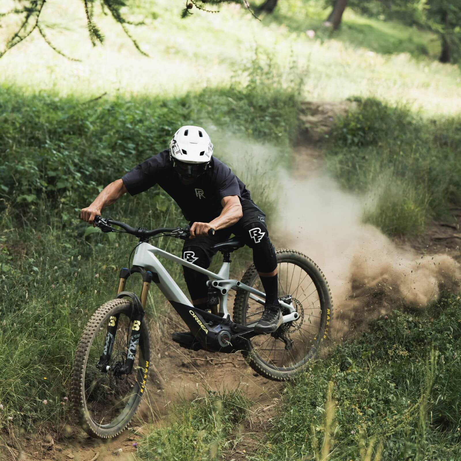 Mountainbiker auf Orbea Wild E-Mountainbike fährt durch Waldweg, wirbelt Staub auf, geeignet für Offroad-Abenteuer.