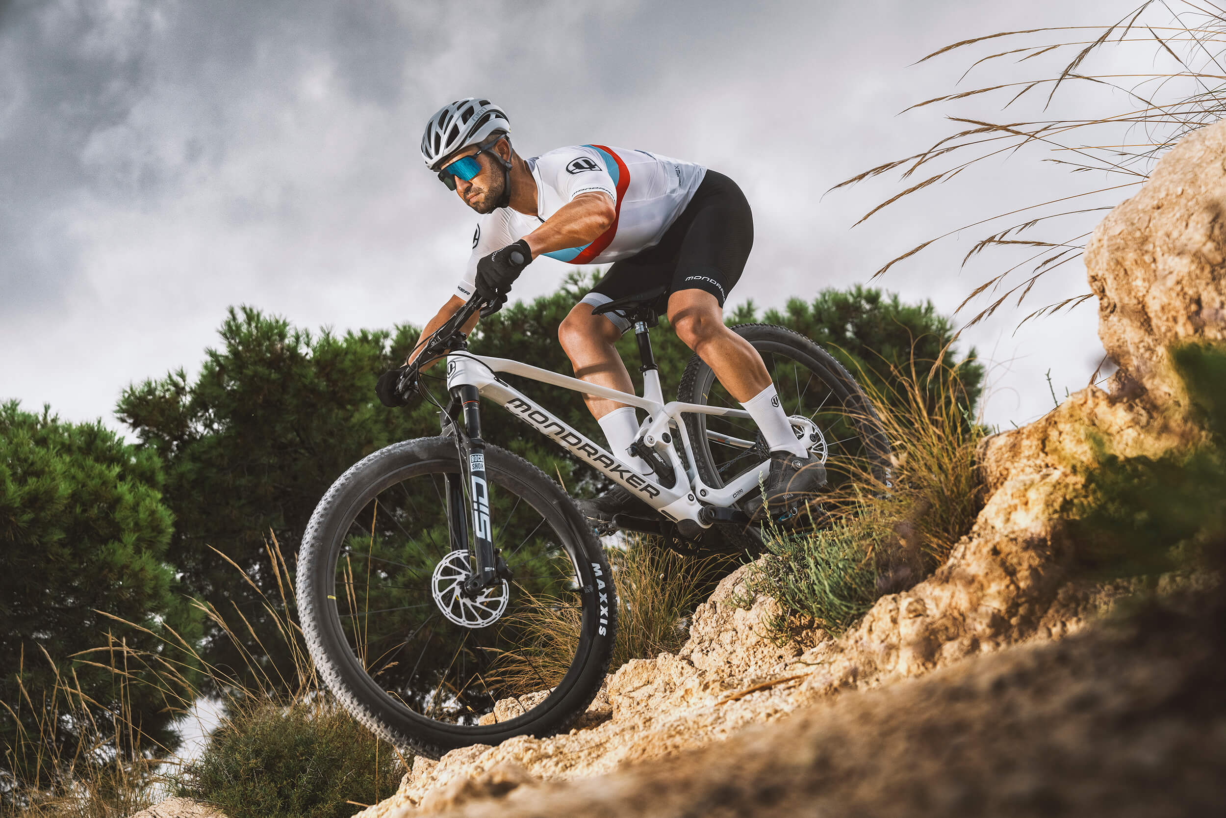 Mann auf Mondraker-Mountainbike fährt steinigen Hügel hinab, geeignet für Offroad-Abenteuer und sportliche Radfahrer.