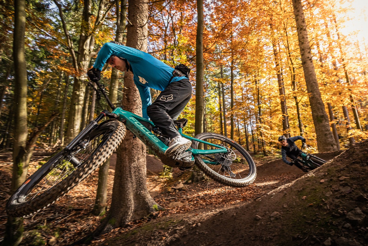 Zwei Personen fahren auf Focus E-Mountainbikes in einem herbstlichen Wald, ideal für Offroad-Fans.