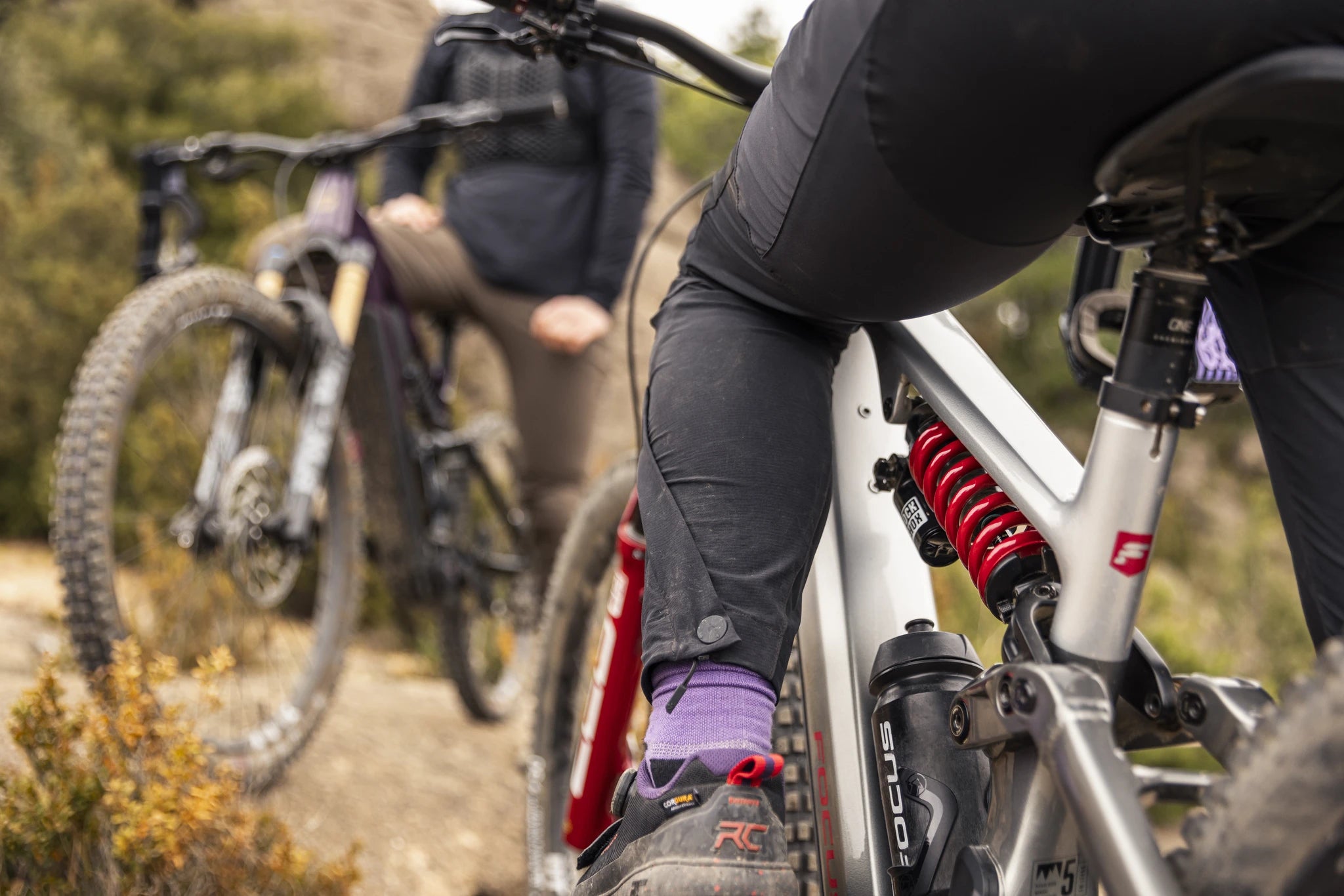 Zwei Personen mit Focus E-Mountainbikes, Modell SAM², unterwegs auf einem steinigen Outdoor-Pfad.