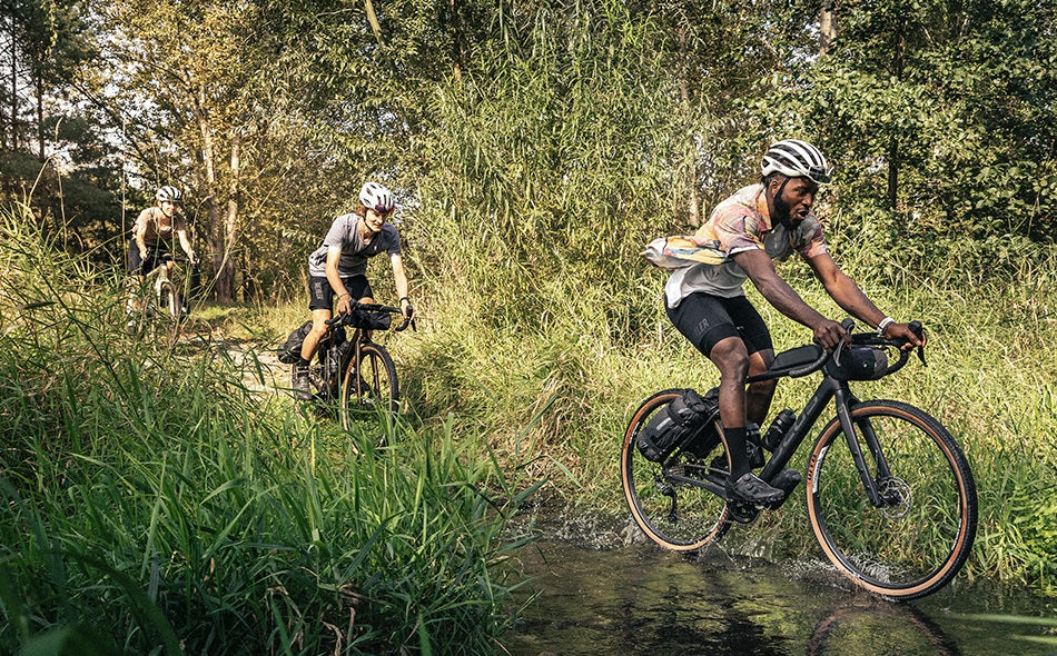 Radfahrer auf Gravelbikes fahren durch dichten Wald, gut für Offroad-Abenteuer. Markennamen und Modell nicht erkennbar.