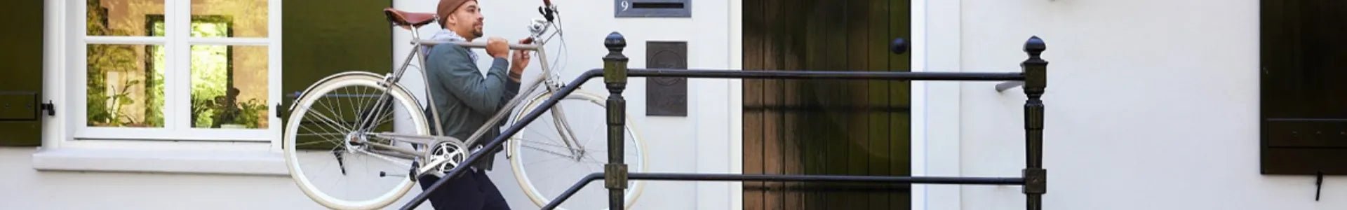 Mann trägt Gazelle Fahrrad über Treppe vor einem weißen Haus mit grünen Fensterläden. Ideal für Stadt- und Freizeitfahrer.