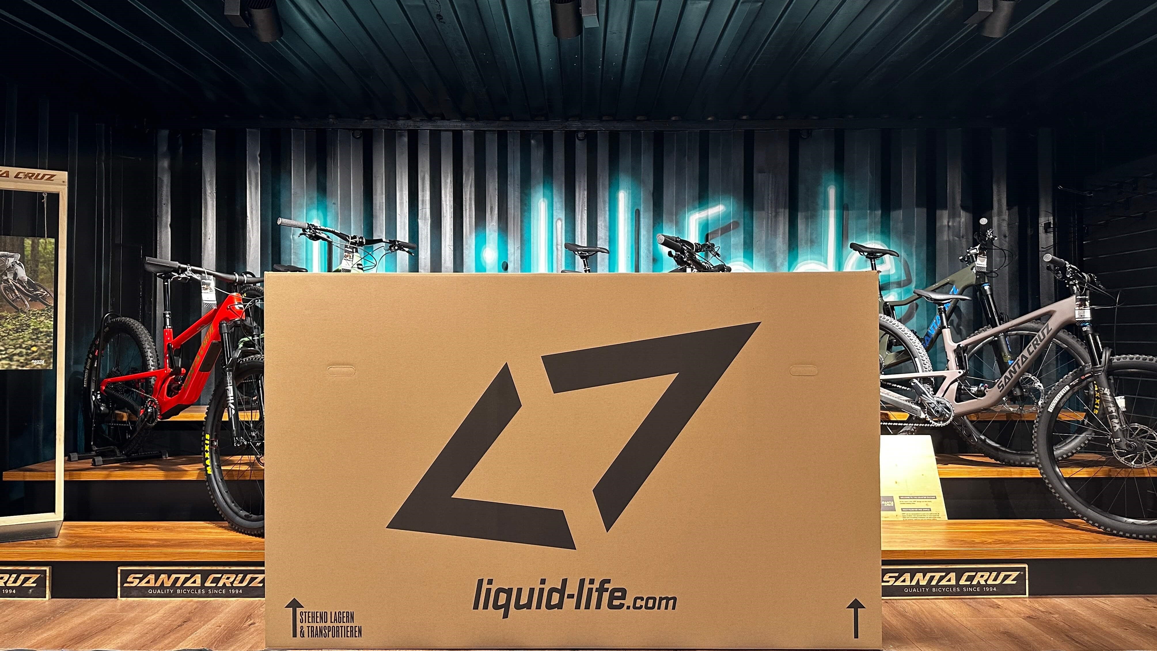 Großer Versandkarton von liquid-life.com vor ausgestelltem Santa Cruz Mountainbike im Showroom.