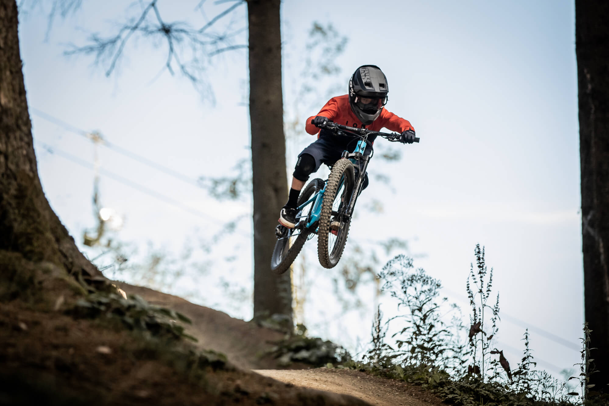 Kind in rotem Shirt und Helm springt mit Mountainbike im Wald. Perfekt für junge Offroad-Abenteurer, 8 Jahre.