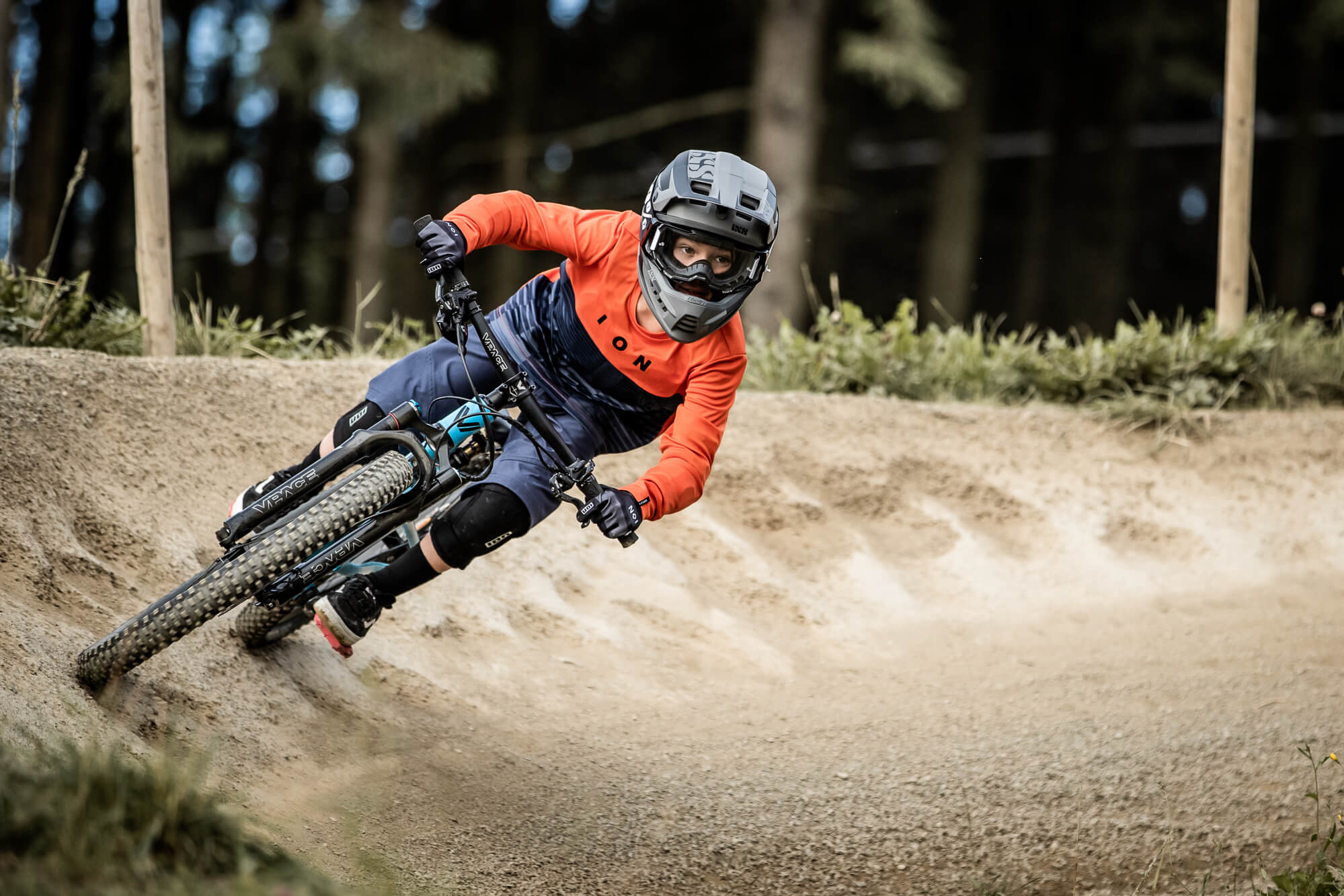 Mountainbiker in rotem ION-Shirt und Helm, fährt Kurve auf staubigem Trail im Wald. Suitable für Adventure-Einsatz.