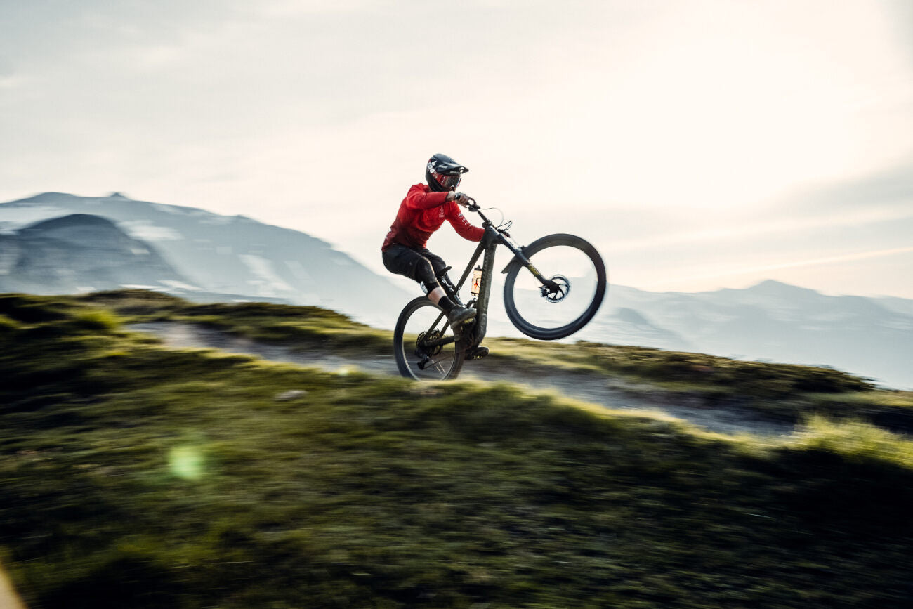 Sportler fährt Specialized E-Bike auf bergigem Gelände bei Sonnenuntergang, geeignet für Mountainbike-Enthusiasten.