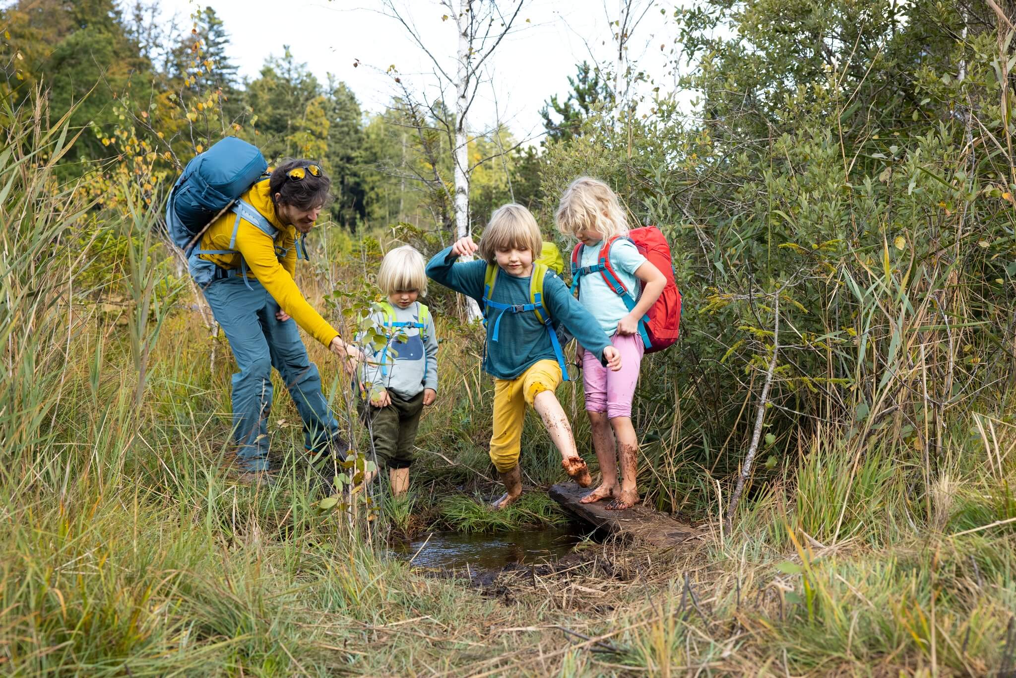 Kinder mit bunten Rucksäcken und Erwachsenen beim Wandern in einem Wald. Ideal für Outdoor-Abenteuer.