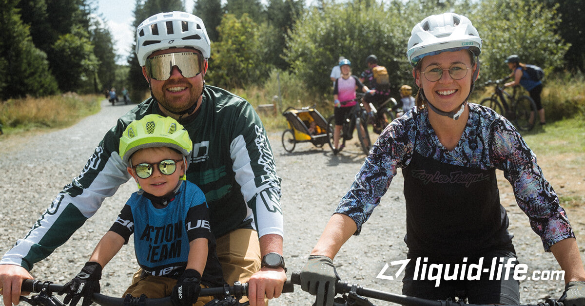 Familie mit Fahrrädern auf einem Feldweg; alle tragen Helme; geeignet für Outdoor-Aktivitäten mit Kindern.