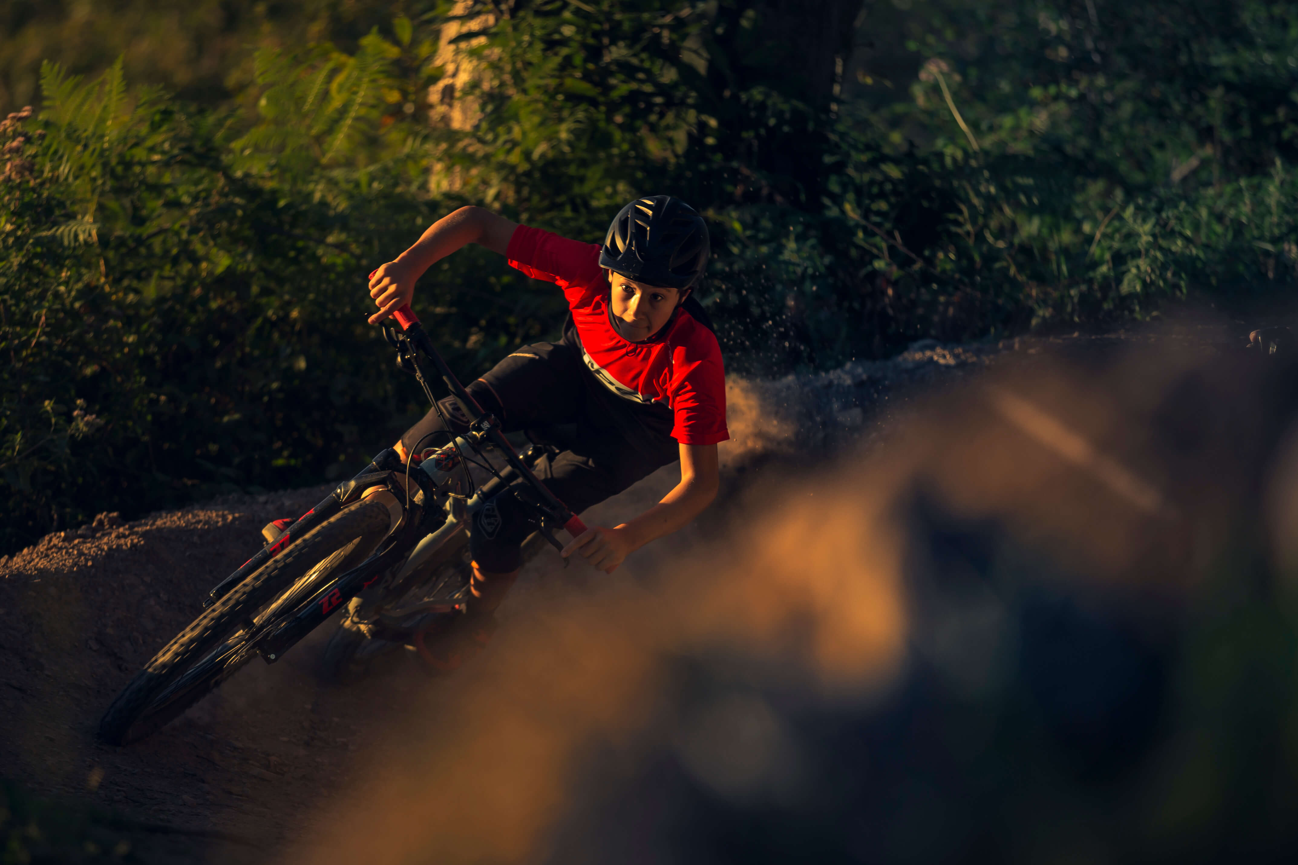 Junger Biker in rotem Oberteil fährt ein Mountainbike in einem Wald.