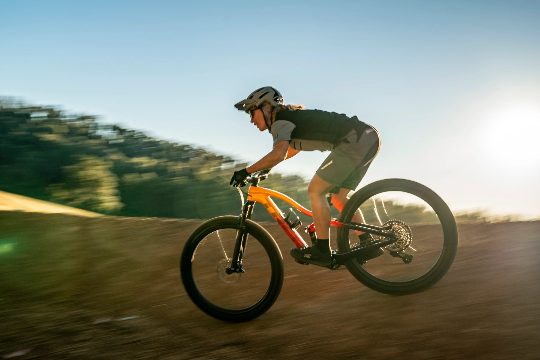 Person auf einem Trek-Fully-Mountainbike fährt mit Helm auf rauem Gelände bei Sonnenuntergang.