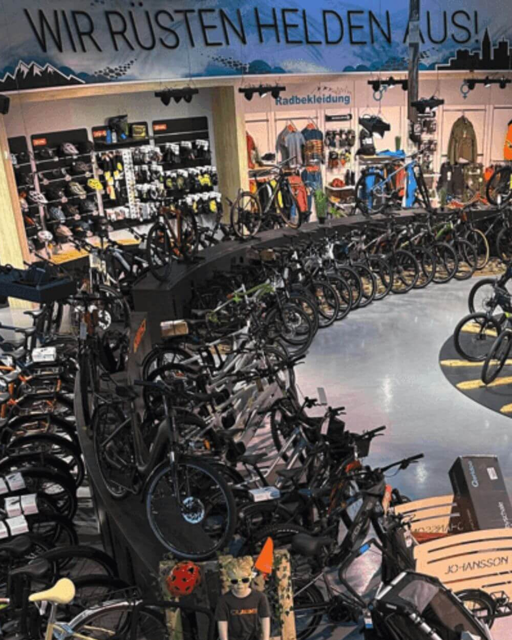 Fahrradgeschäft mit großer Auswahl an Fahrrädern und Zubehör, Schild "Wir rüsten Helden aus" über Verkaufsfläche.