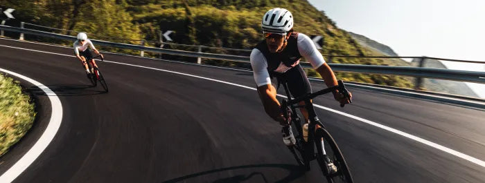 Zwei Superior Radfahrer in Rennbekleidung fahren schnell eine kurvige, asphaltierte Straße in bergiger Landschaft hinunter.