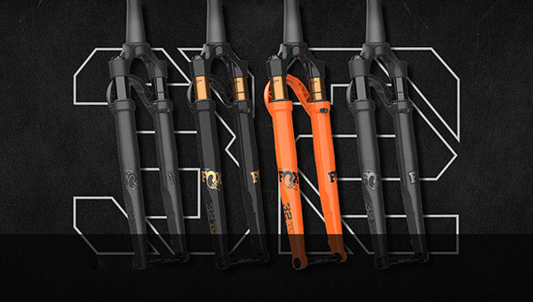 Vier FOX-Fahrradgabeln in Schwarz und Orange, geeignet für Mountainbikes, vor schwarzem Hintergrund platziert.