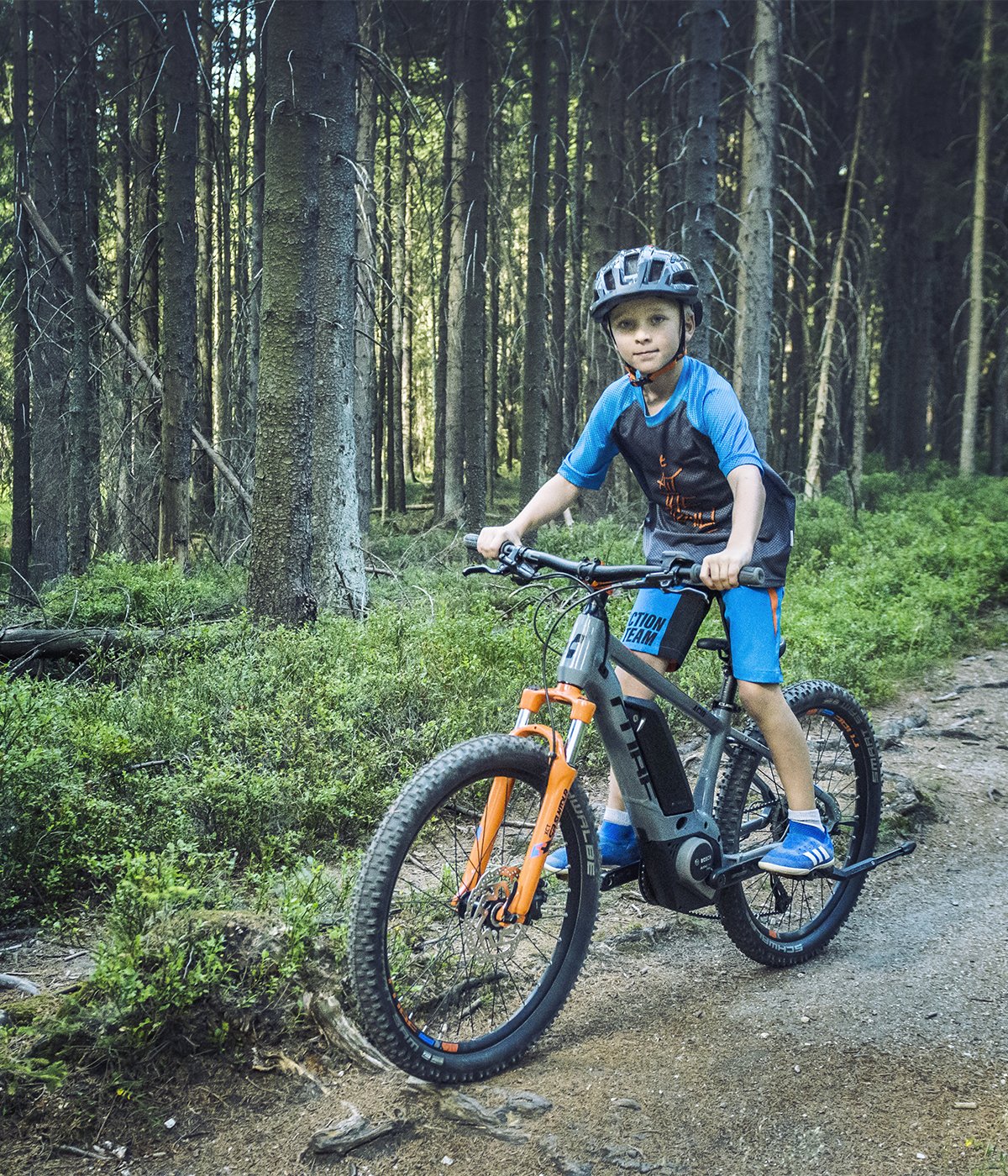 Kind auf einem Kinder-E-Bike im Wald, trägt Helm und Sportkleidung. E-Bike für junge Abenteurer.