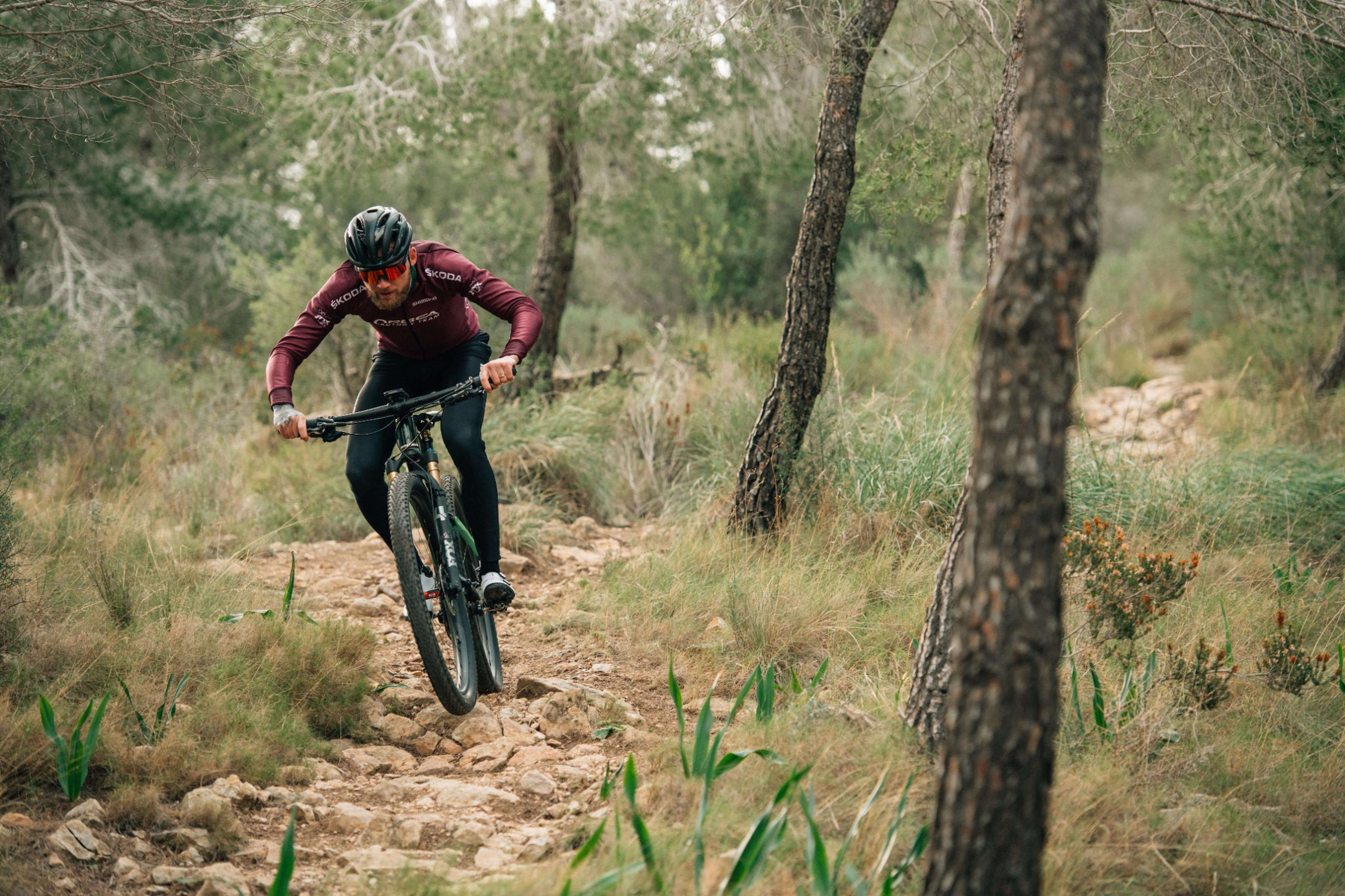 Mountainbiker fährt ein Orbea Oiz auf einem steinigen Waldweg, trägt roten Anzug und Helm. Sportliche Outdoor-Aktivität.
