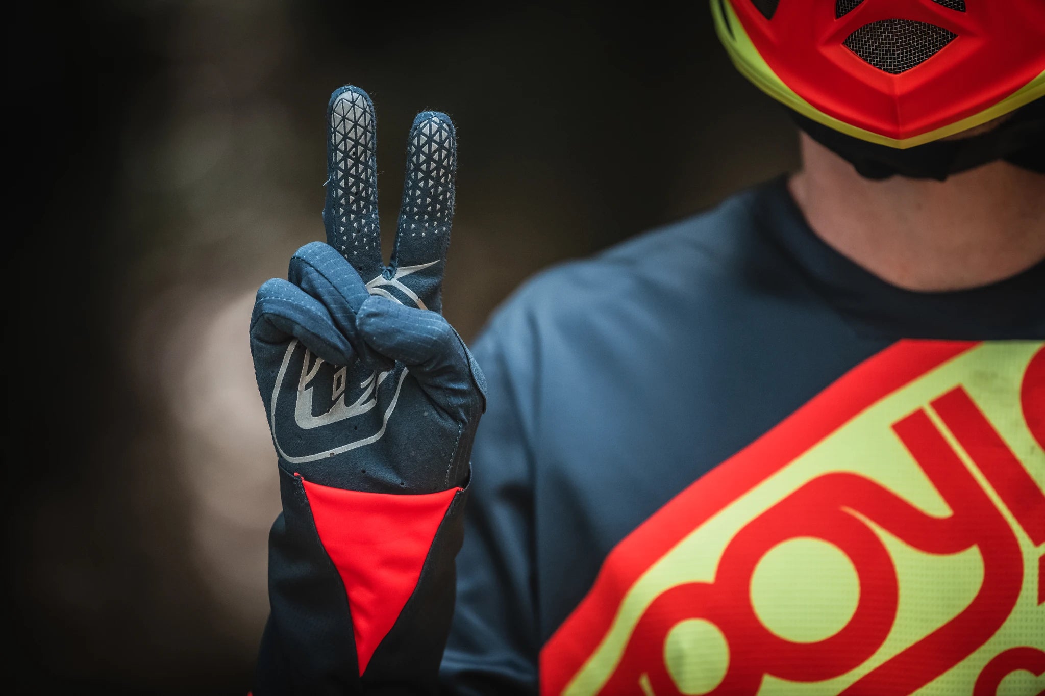 Blauer Fahrradhandschuh mit rotem Akzent, Helm sichtbar, Person zeigt Peace-Zeichen. Ideal für Motocross-Enthusiasten.