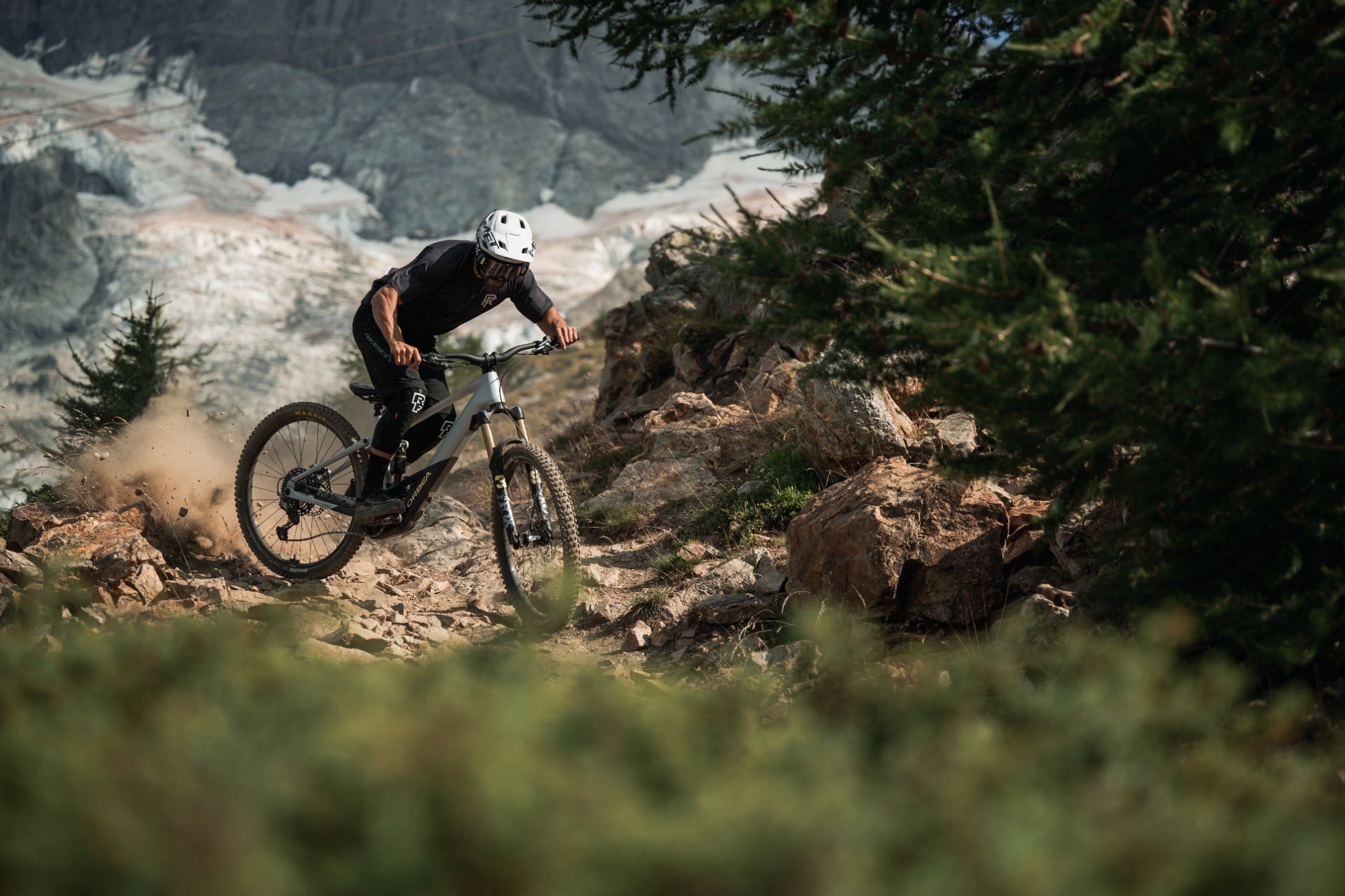 Mountainbiker fährt auf felsigem Pfad mit Orbea Wild E-Mountainbike, umgeben von Naturkulisse, Helm tragend.