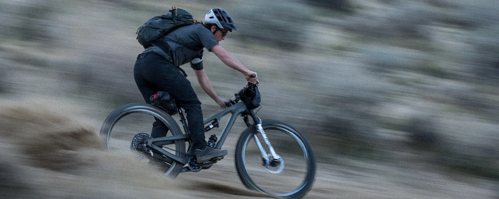 Mann fährt mit Mountainbike und Helm über Gelände, seitliche Ansicht. Ideal für Outdoor-Enthusiasten.
