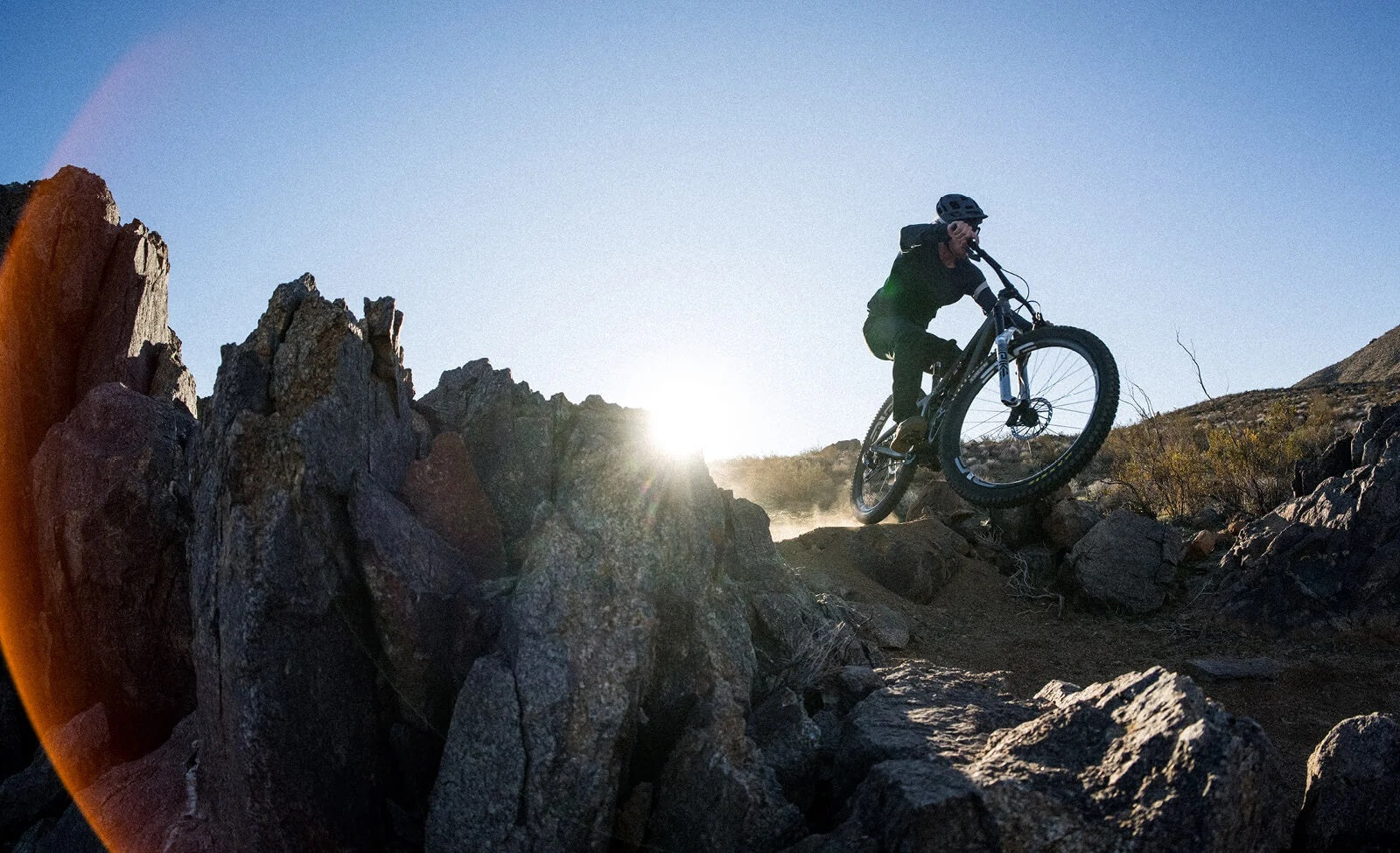 Radfahrer springt mit Mountainbike über Felsen im Gelände bei Sonnenuntergang; geeignet für Outdoor-Abenteuer.