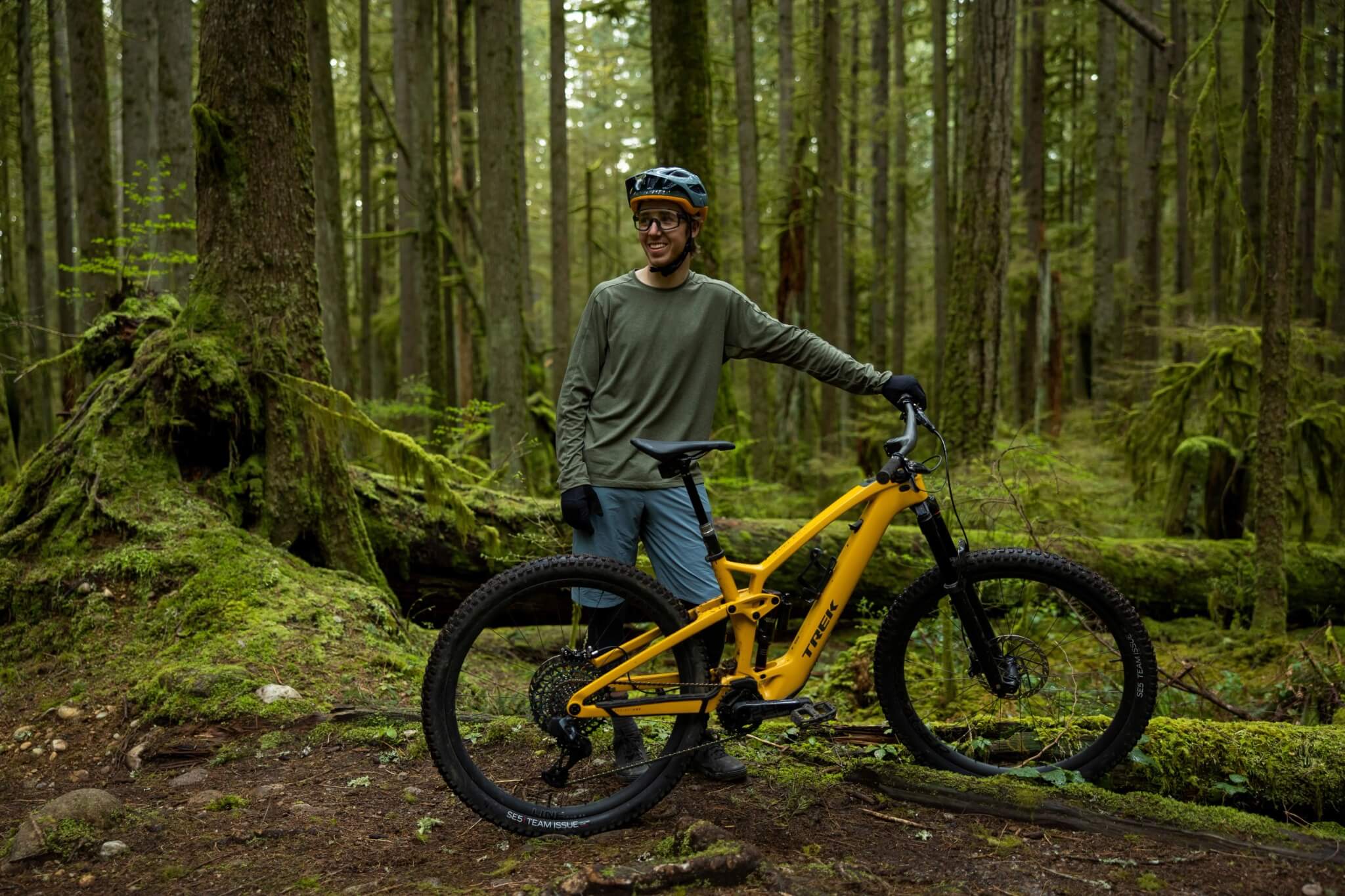 Mann im Wald mit gelbem Trek E-Bike, ideal für Mountainbiking, neben ihm.