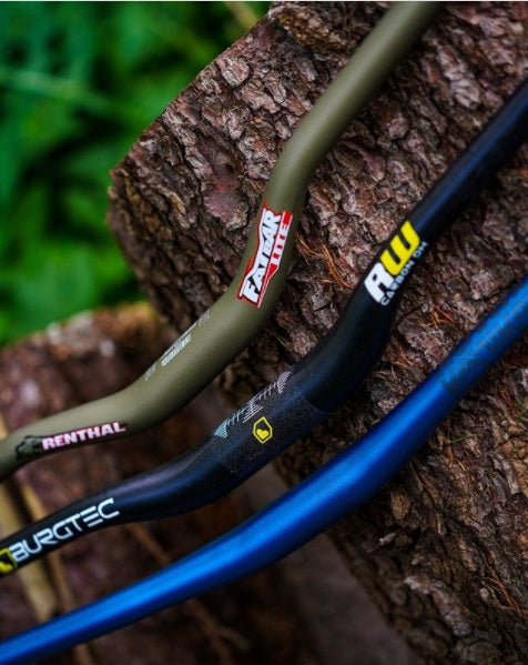 Drei Fahrradlenker von Renthal, Burgtec und Fatbar, auf einem Baumstamm im Freien platziert.